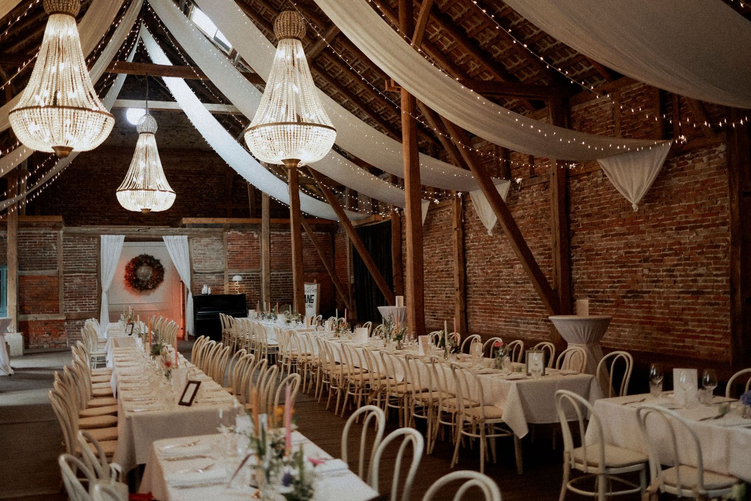 Elegant wedding reception venue with crystal chandeliers, exposed brick walls, and white drapery decorations. Rittergut Falkenhardt.