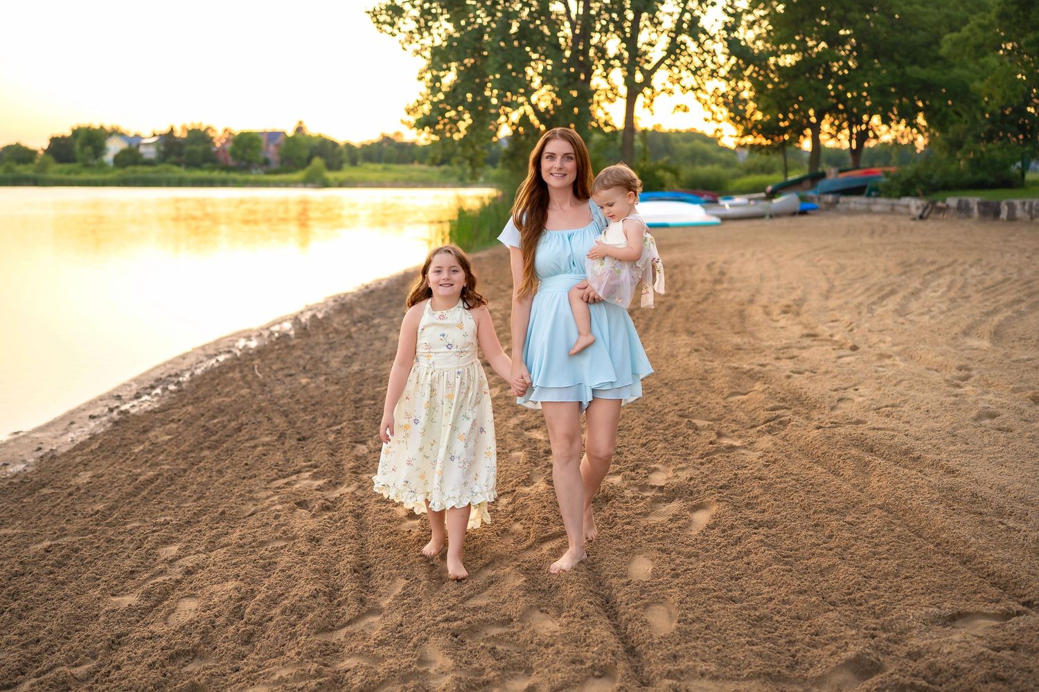 Three people walking along a sandy beach at sunset with a golden lake in the background.