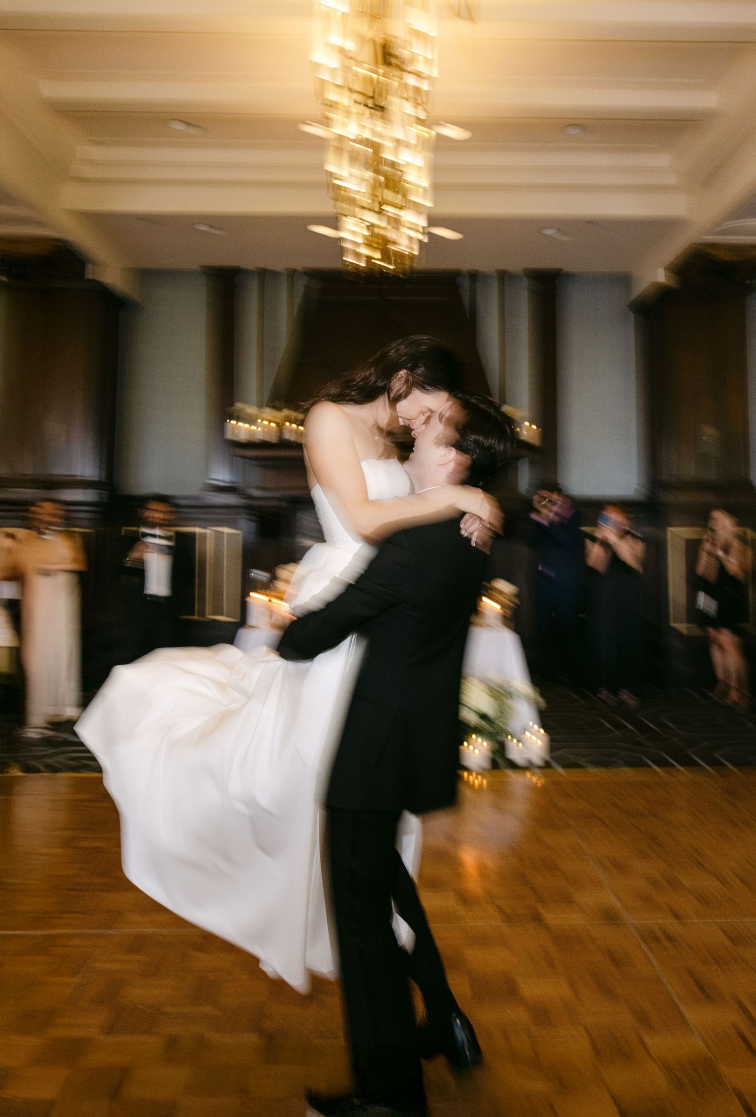 A couple shares an intimate moment at an elegant reception dinner table with glowing candles and other guests in background.