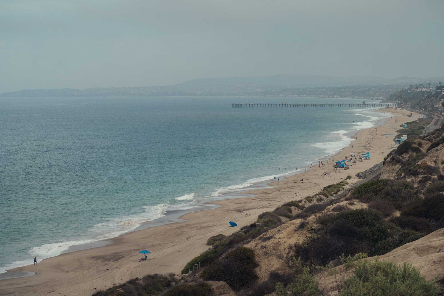 Aerial panoramic view of a sandy beach coastline with turquoise ocean waters and cliffs stretching into the distance.