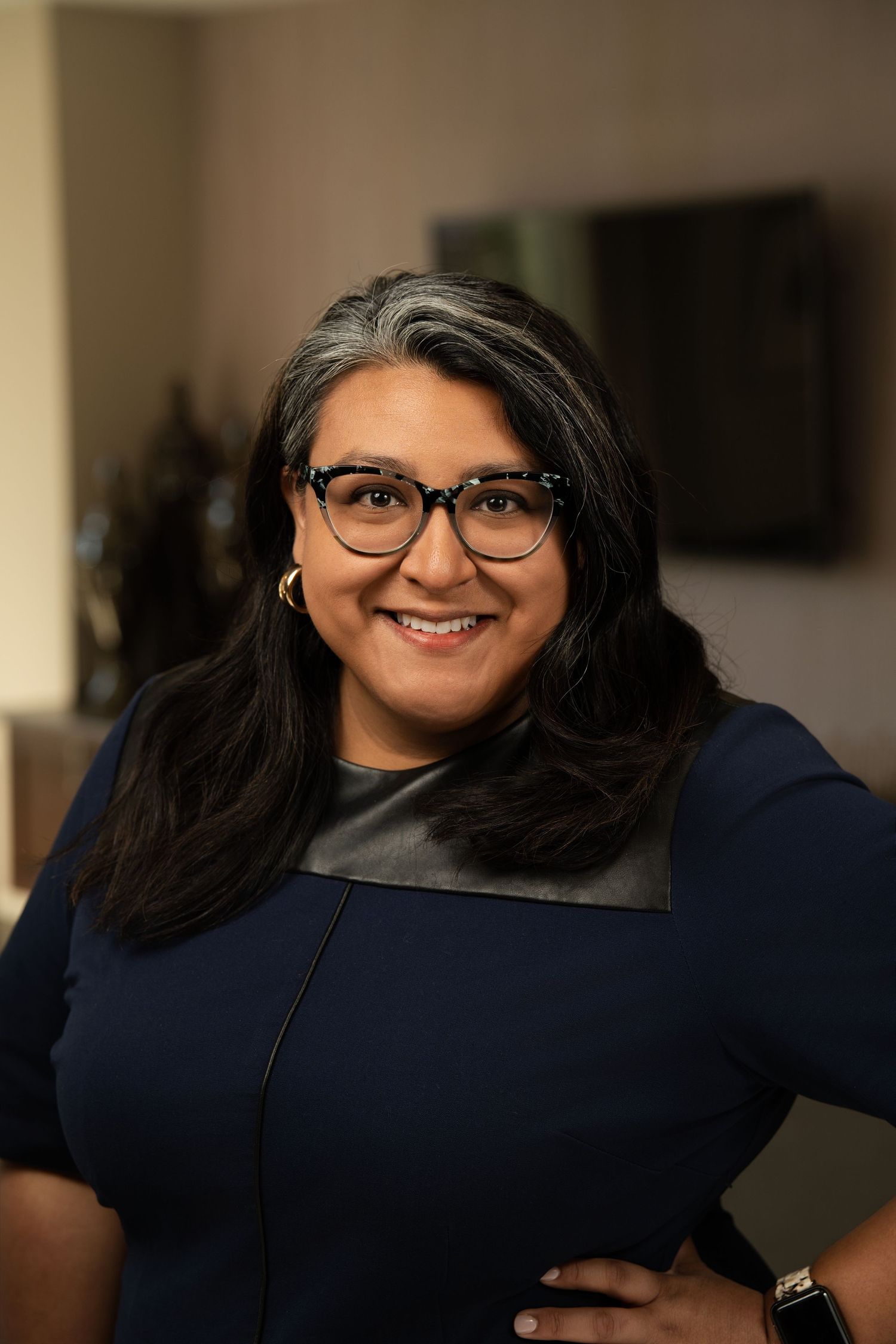 Professional headshot of a person wearing glasses and navy blue top smiling warmly at the camera.