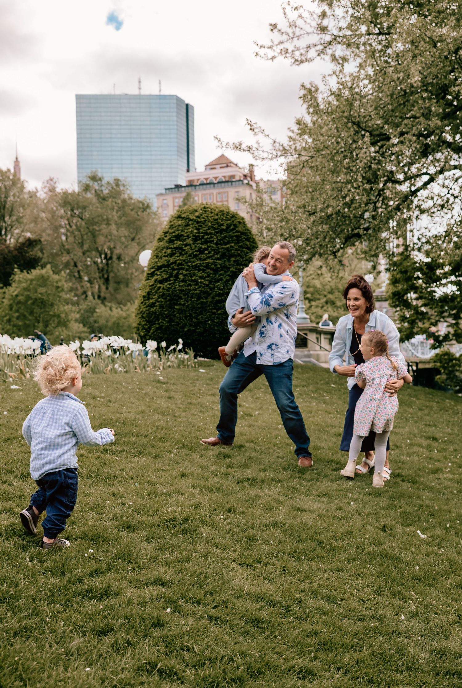 Group plays together joyfully on a grassy hillside, rolling and tumbling while having fun outdoors on a cloudy day.