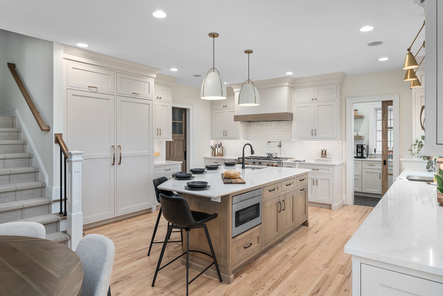 Modern white kitchen with quartz countertops, pendant lights, and hardwood flooring in an open concept layout.