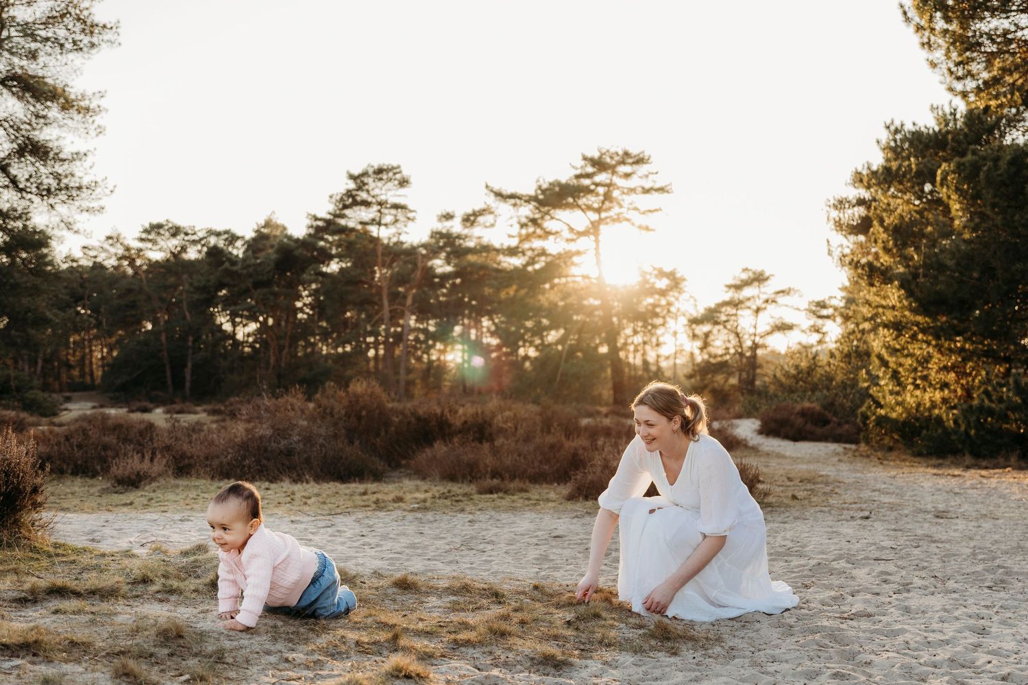moeder en door zand kruipende dochter speelse gezinsfotografie op de soesterduinen met goldenhour