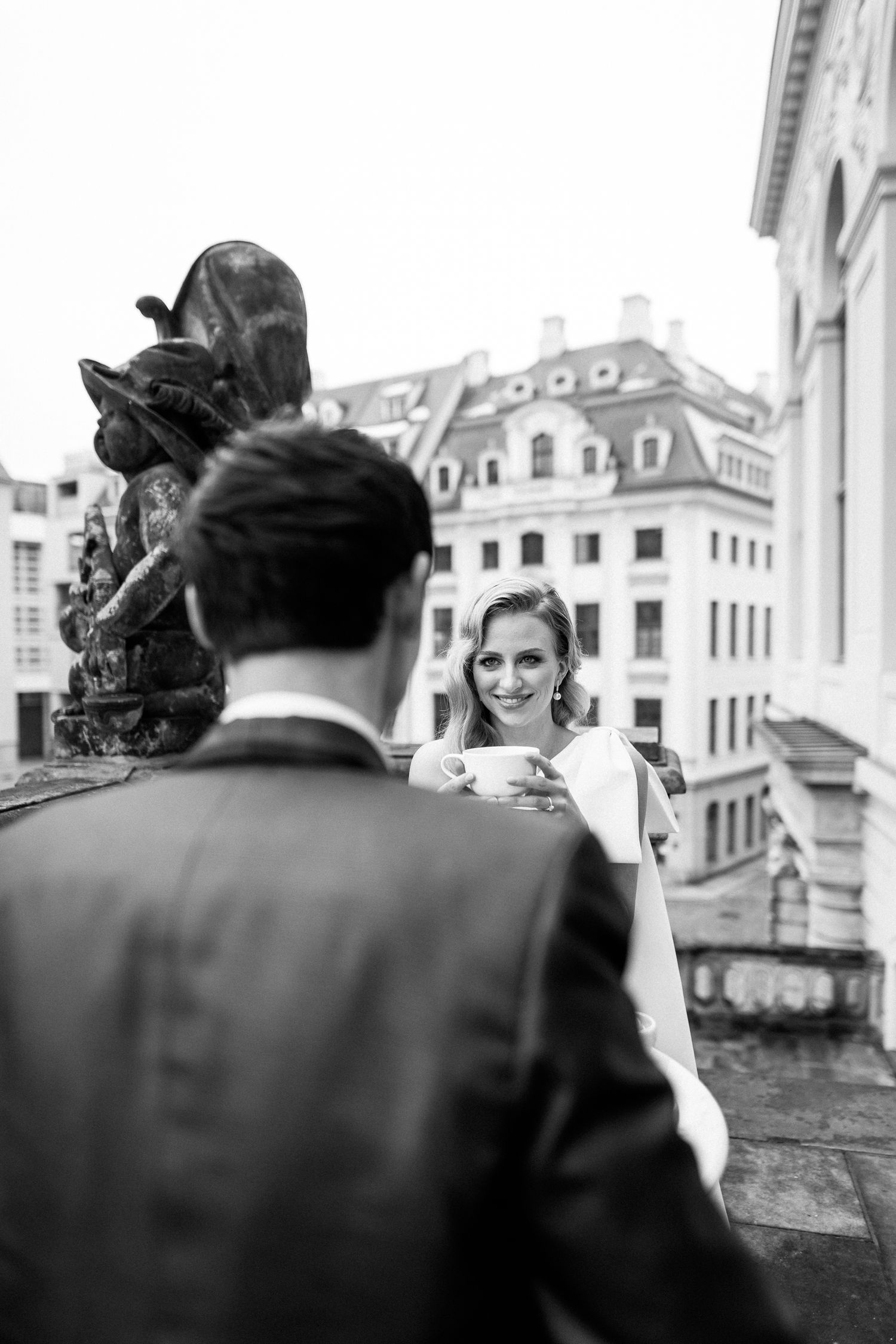 Black and white photo of a couple at their wedding on a European balcony with historic architecture in the background.