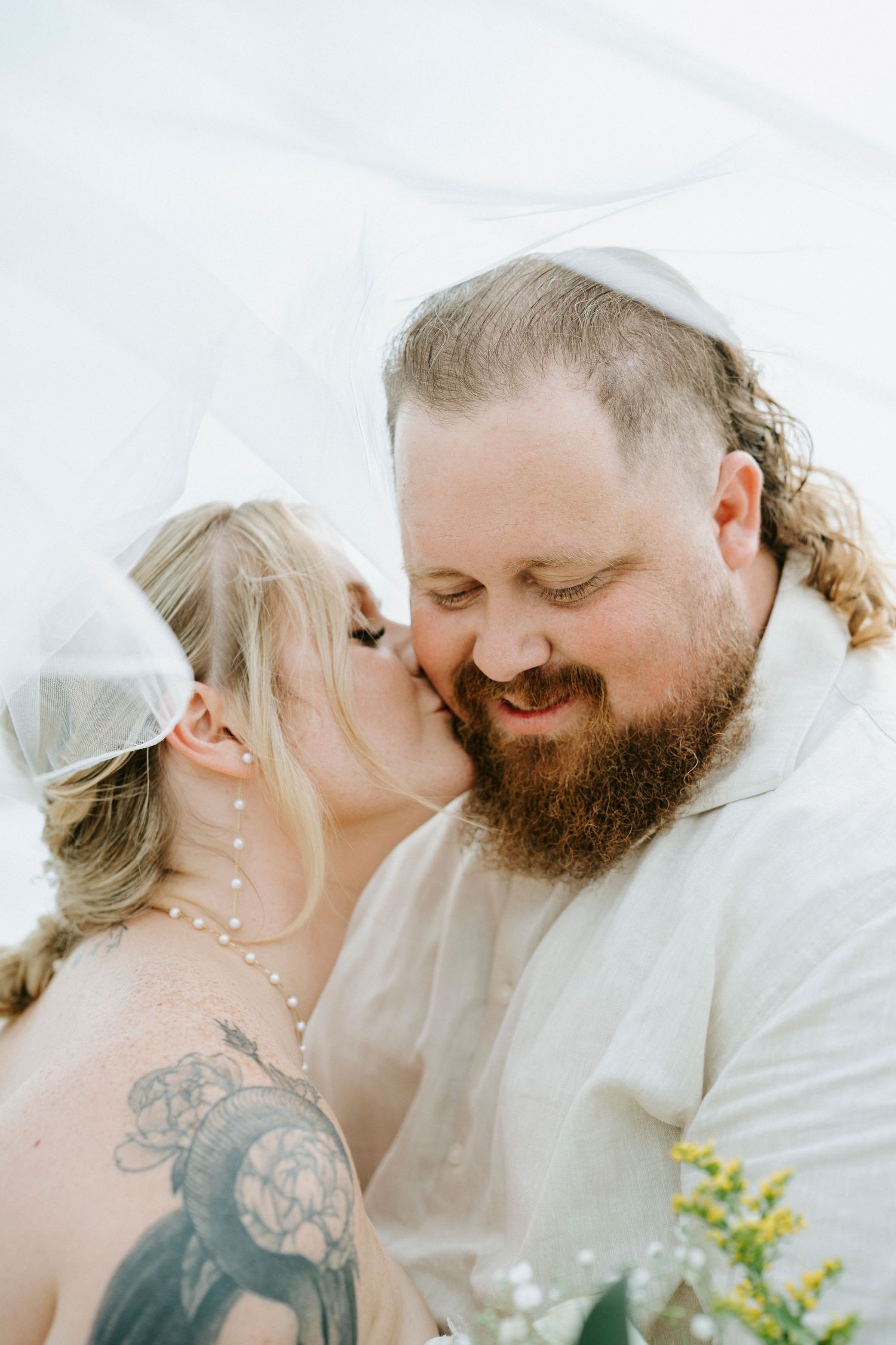 A romantic wedding moment captured under a flowing white veil with soft natural lighting.