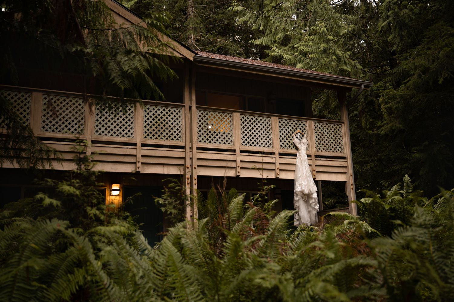 A wedding dress hangs from the porch of a lodge, surrounded by evergreens and ferns at Lake Crescent in Olympic National Park.