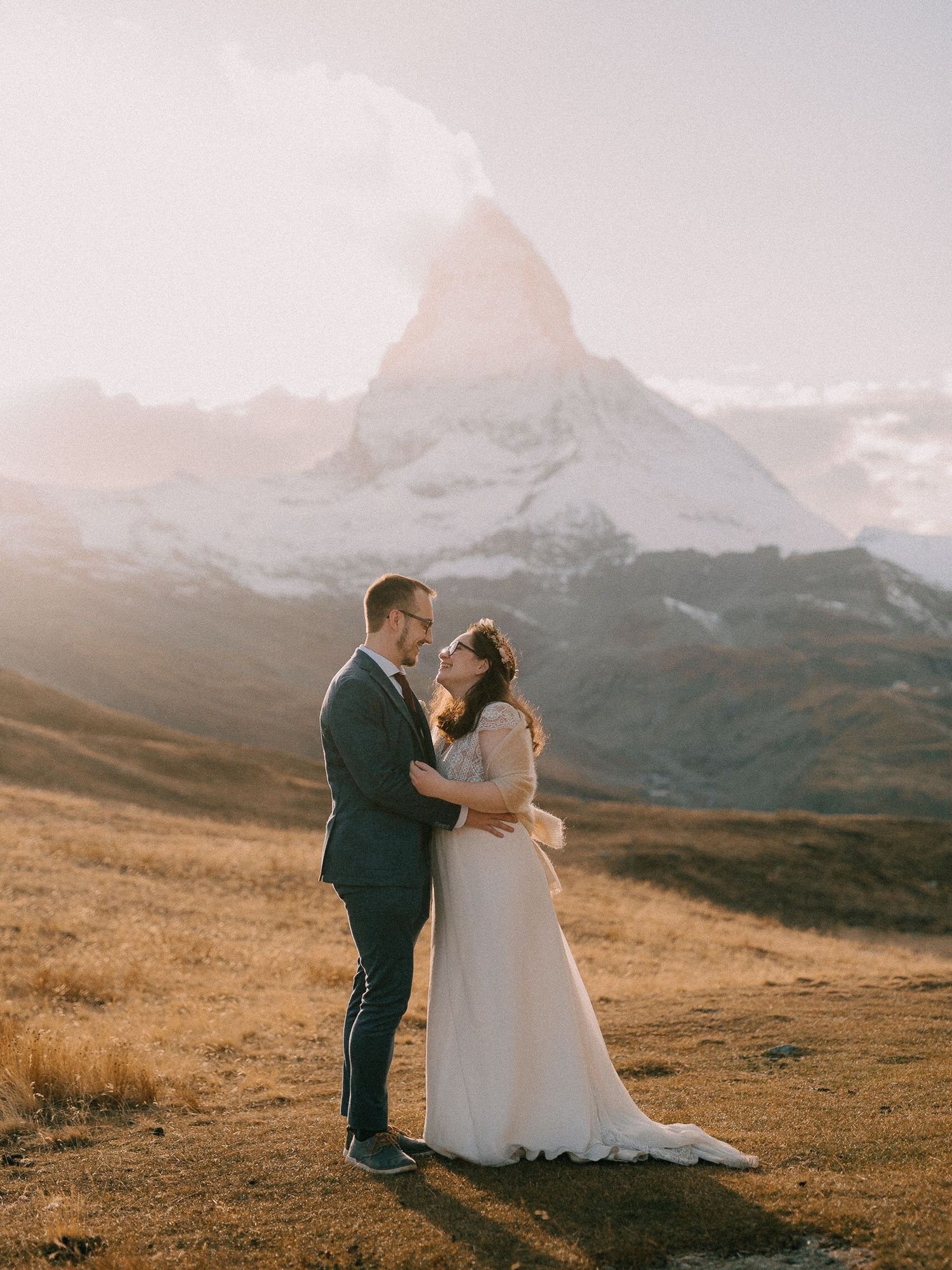 A couple shares a romantic moment in the Swiss Alps during golden hour with majestic mountain peaks in the background.