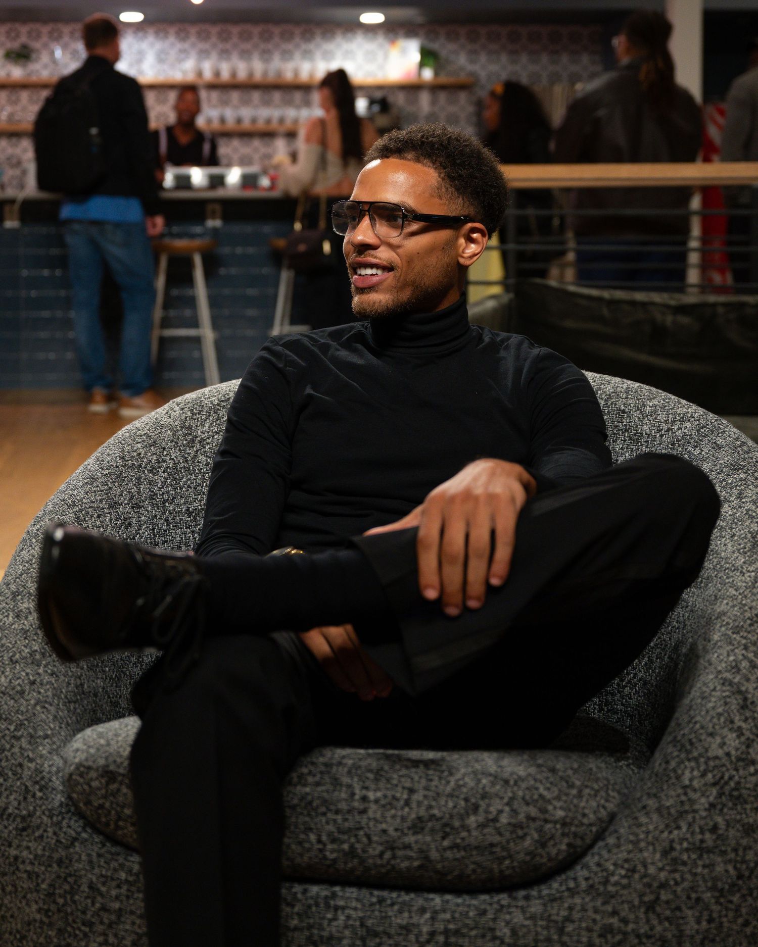 Person in dark clothing relaxes on a textured gray sofa in a dimly lit indoor setting.