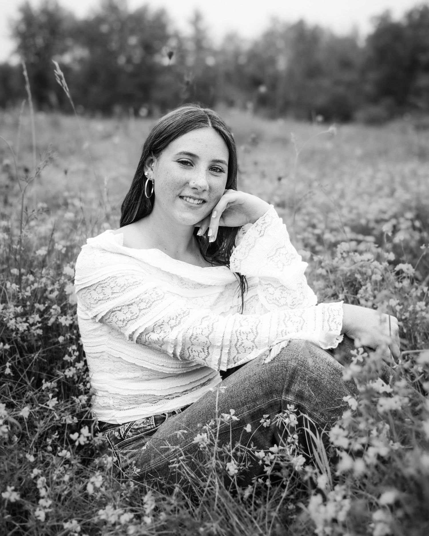 A person in a white sweater sits among wildflowers in a sunny meadow, captured in black and white.