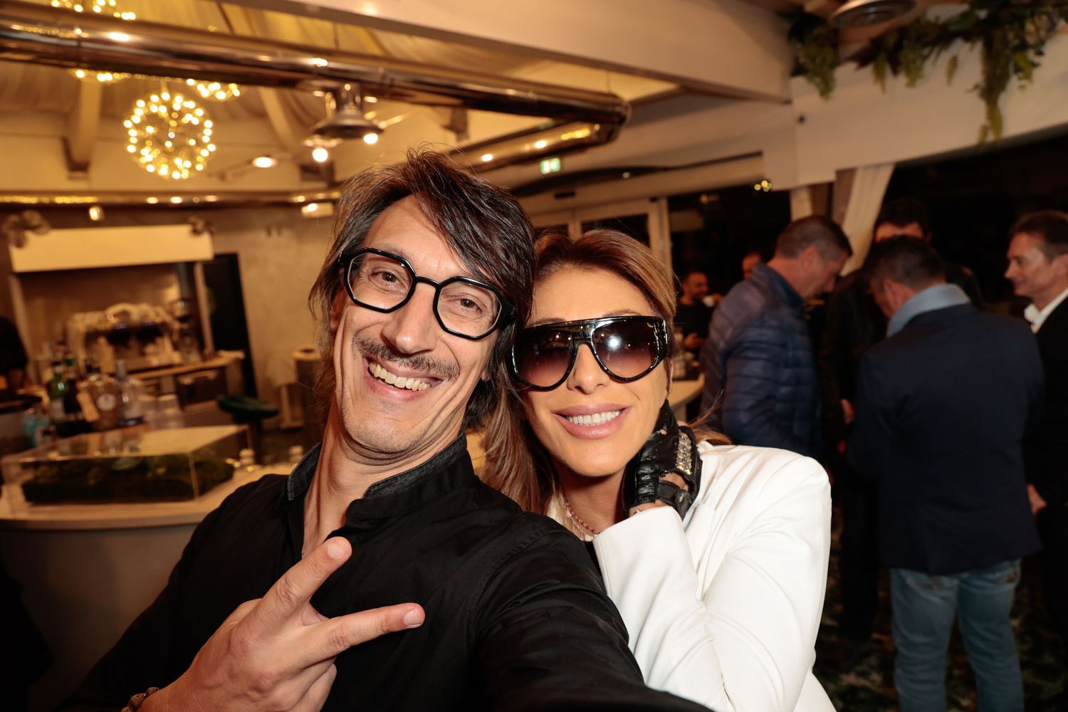 Two people posing together at an indoor event with festive lighting.