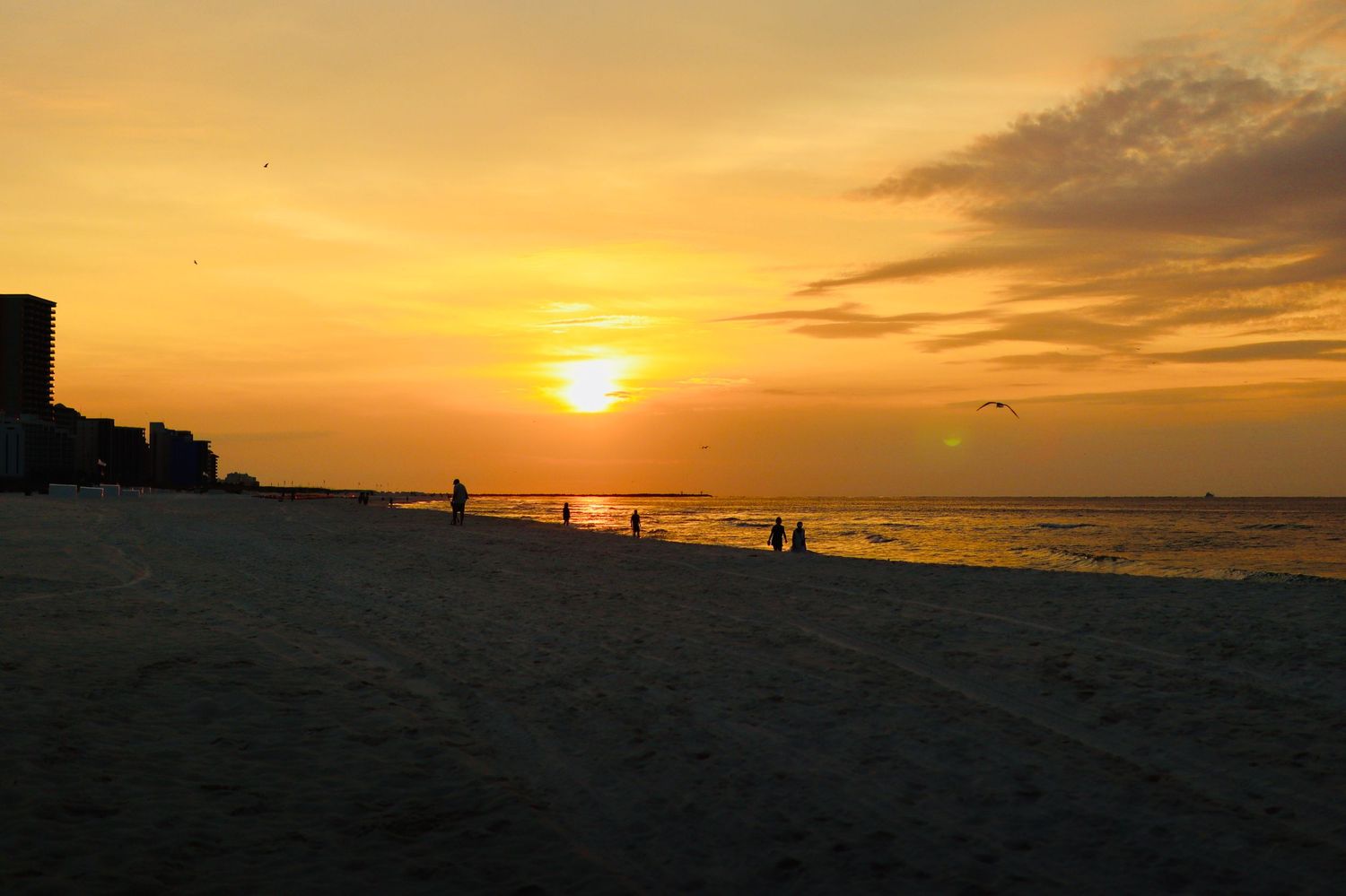 Stunning golden sunset over a sandy beach with silhouettes of people walking along the shoreline.