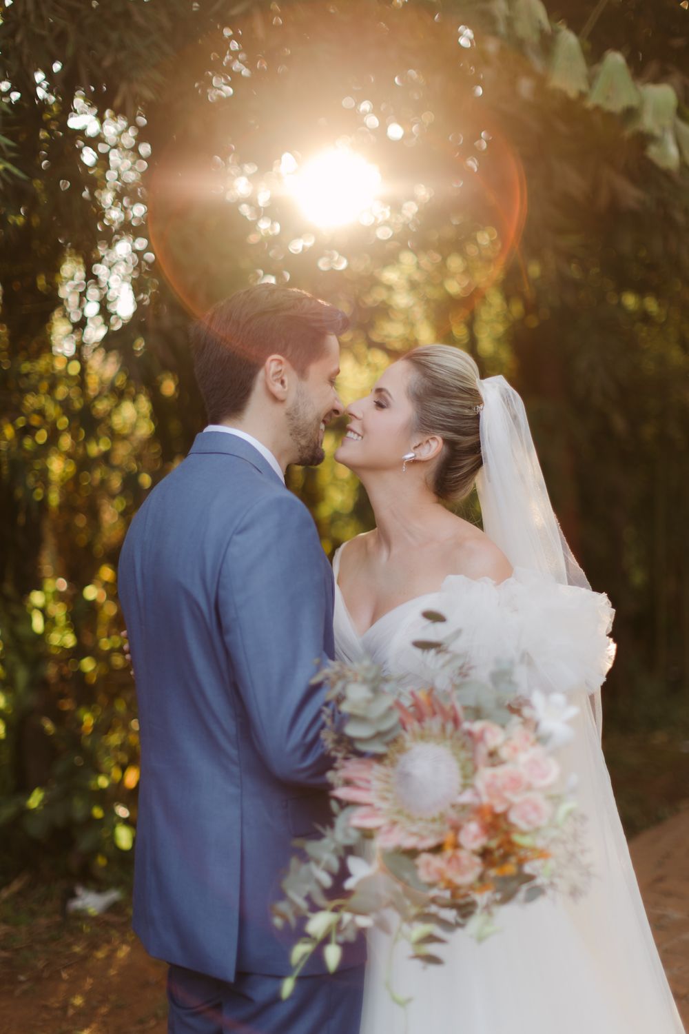 Romantic sunset portrait of bride and groom with glowing backlight and floral bouquet.