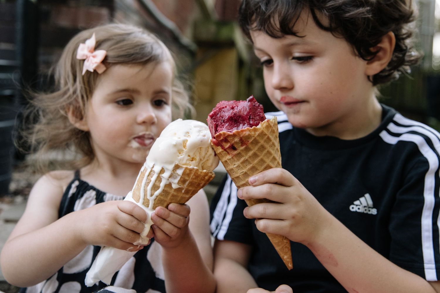 Two children enjoying ice cream cones on a warm day, with one eating chocolate and the other with a vanilla cone.