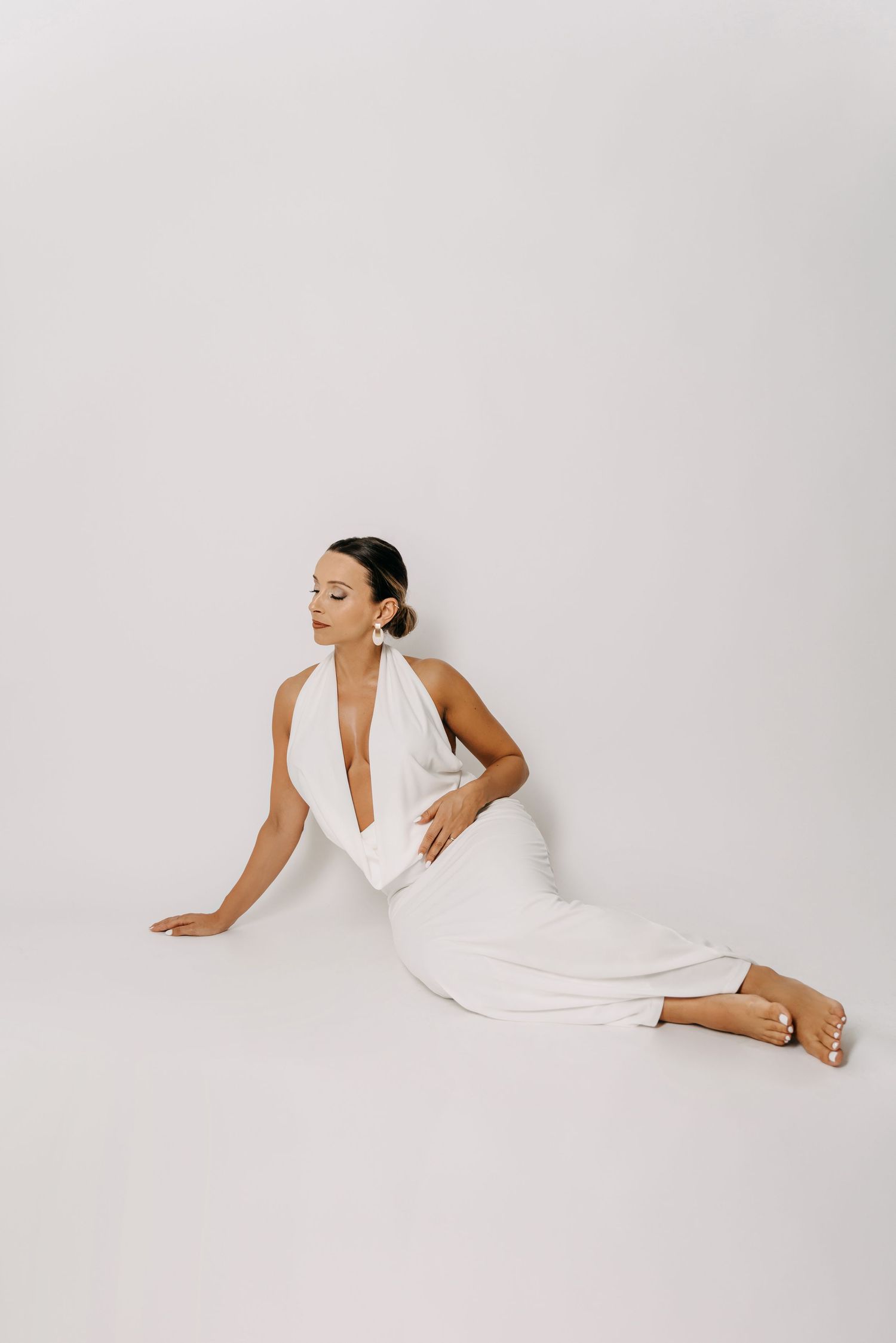 Minimalist fashion photo featuring a sleek white halter dress on a light background.