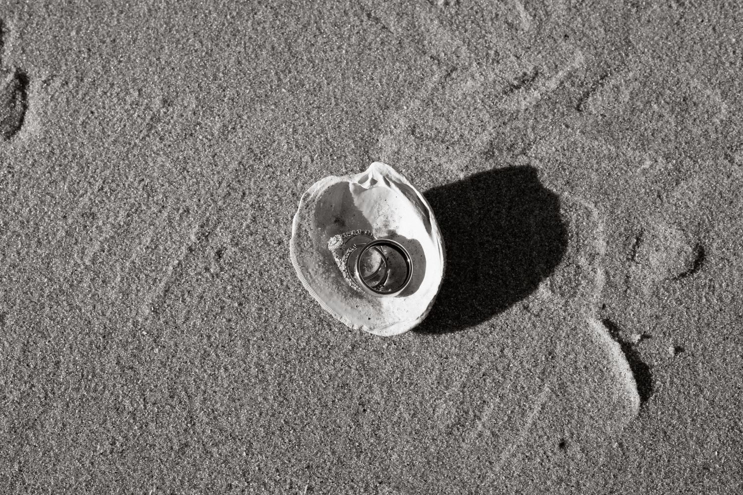 A small clear glass jar casts a dark shadow on textured gray sand at the beach.