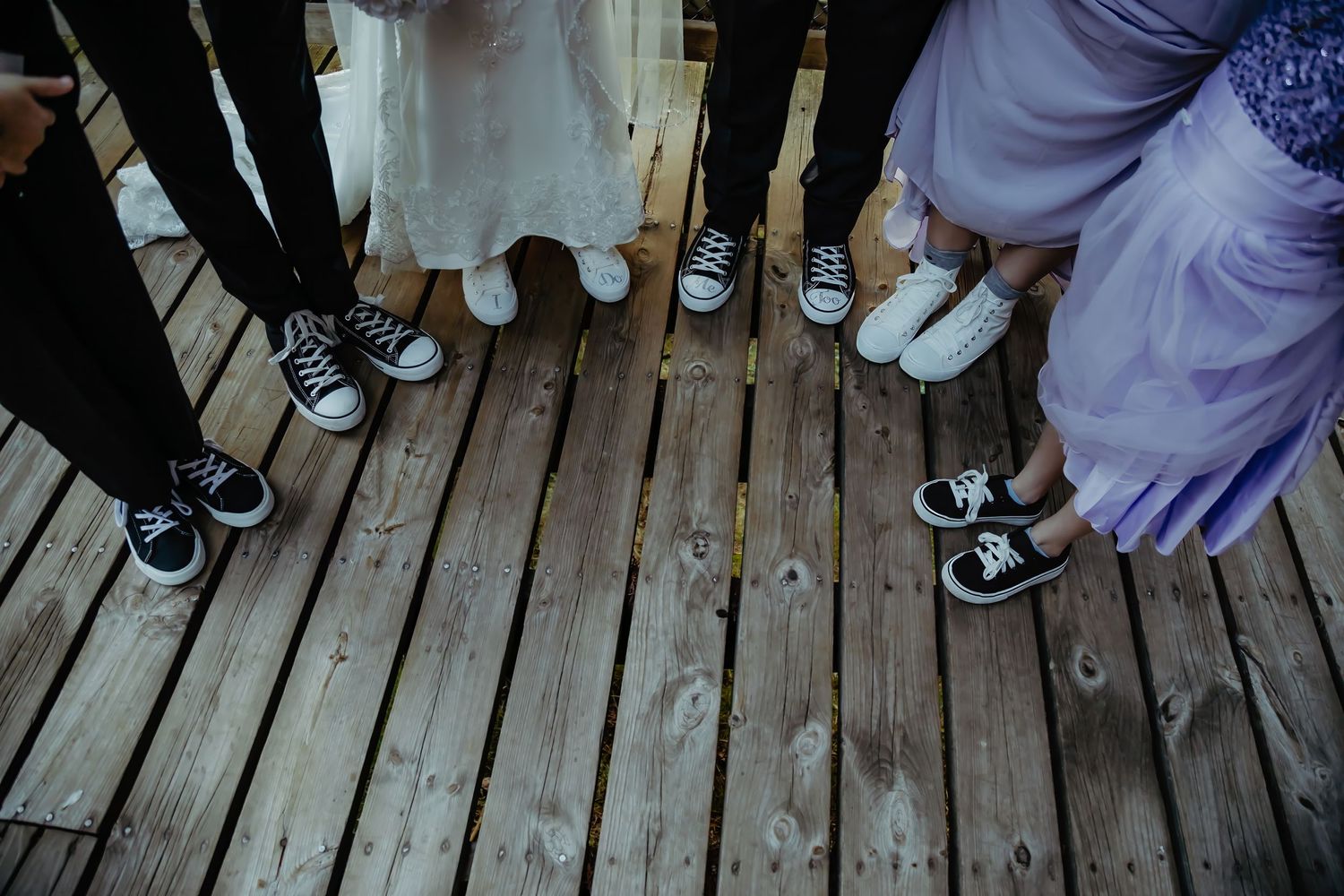 A creative wedding party photo showing everyone's matching Converse sneakers on wooden deck.