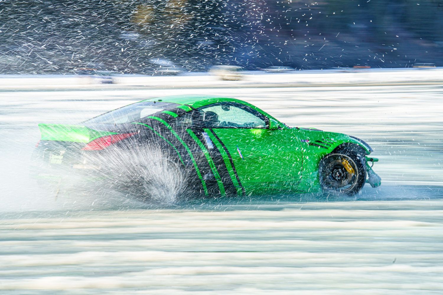 Bright green sports car racing through snowy terrain, kicking up powdery snow spray behind it.