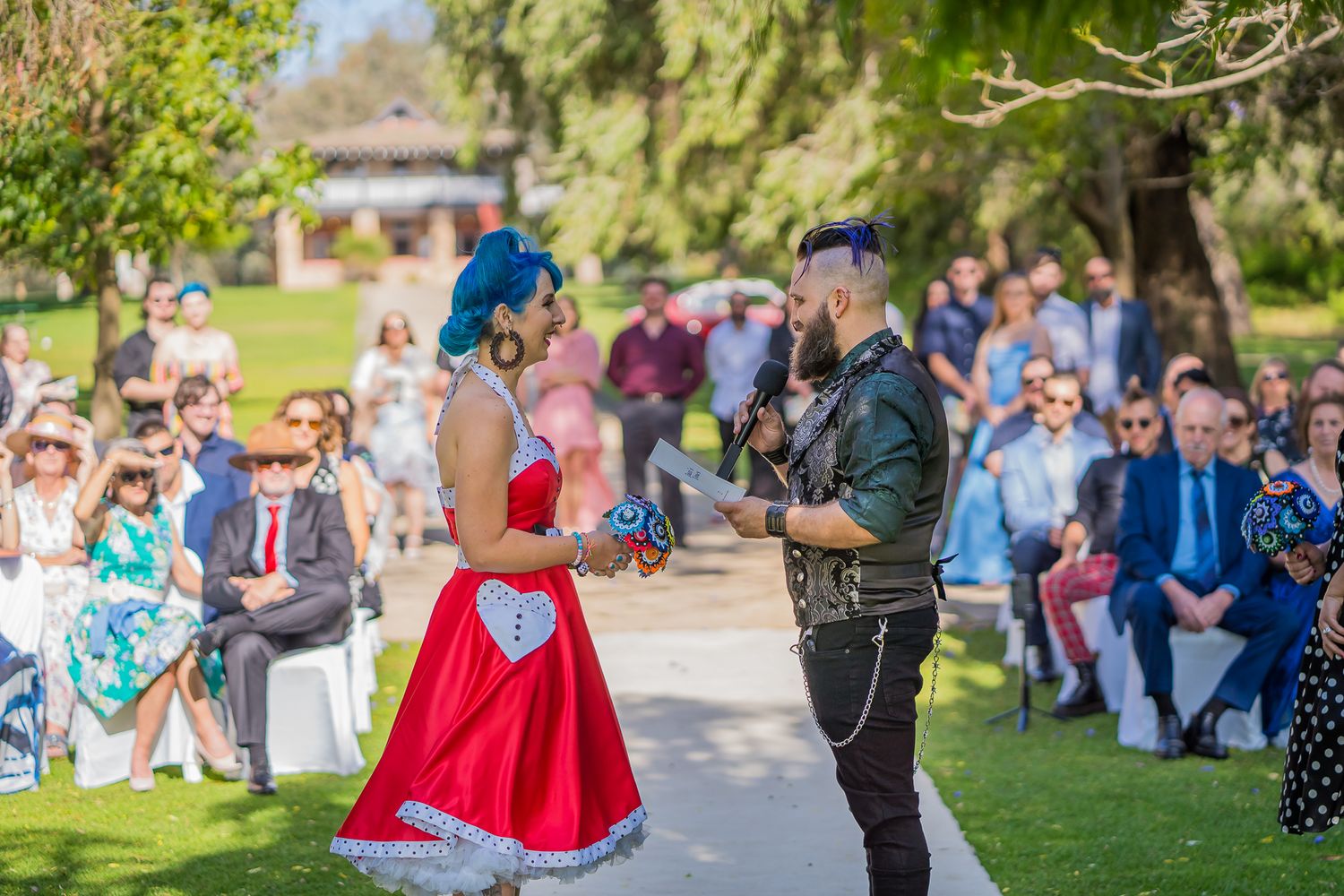 Two people perform an entertaining outdoor dance routine at a summer event while guests watch from lawn chairs and benches.