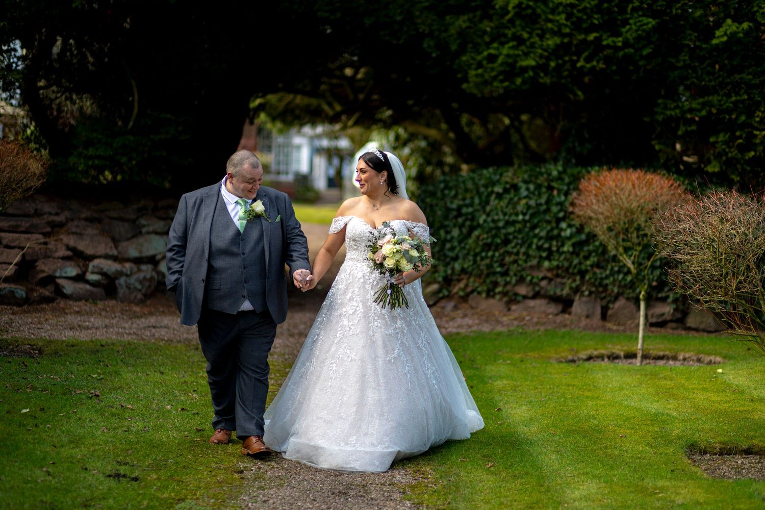 Wedding couple walking through lush garden pathway during outdoor photo session.