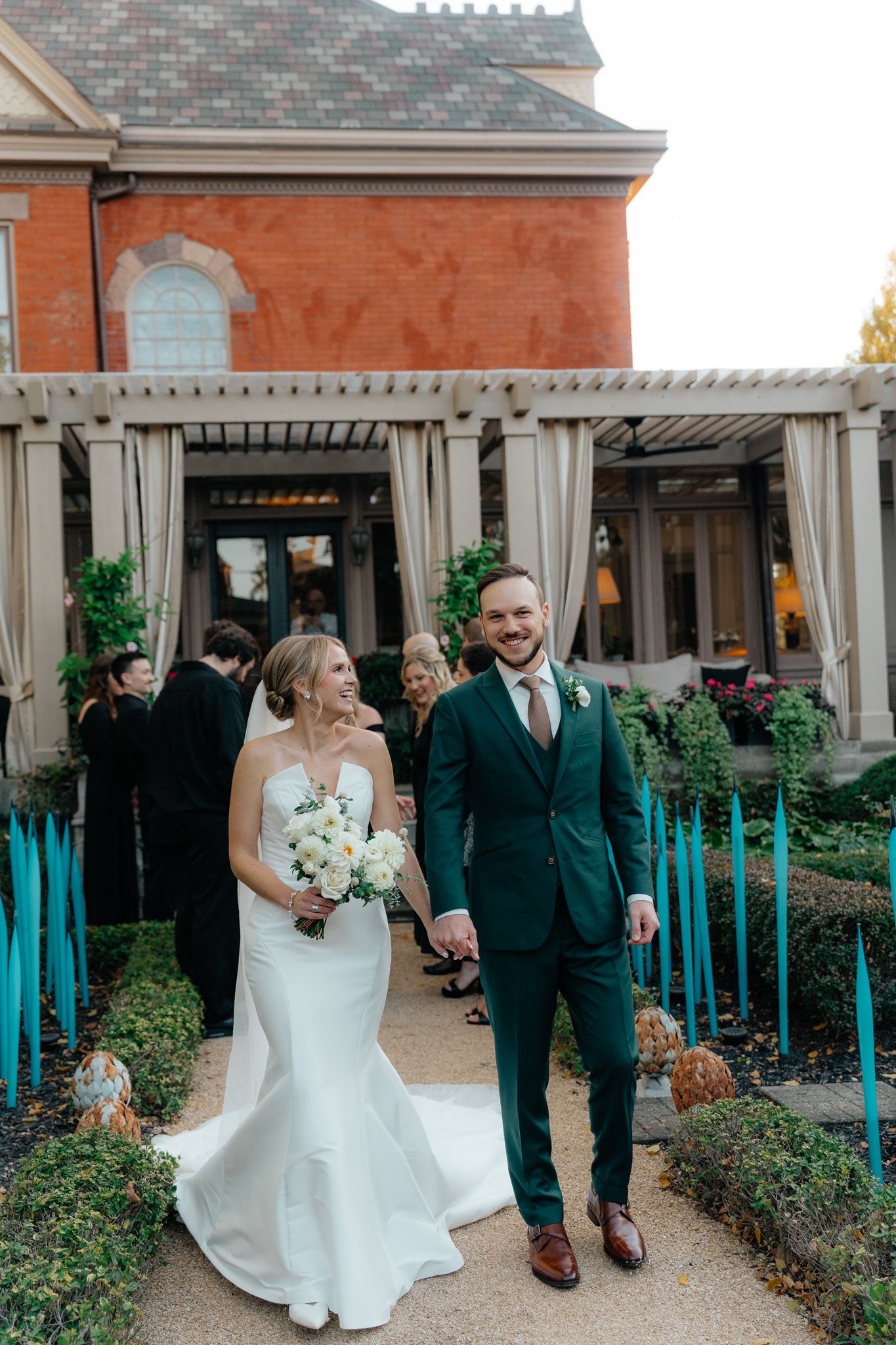 Couple celebrating their wedding day walking under a pergola decorated with blue light accents at a historic venue.