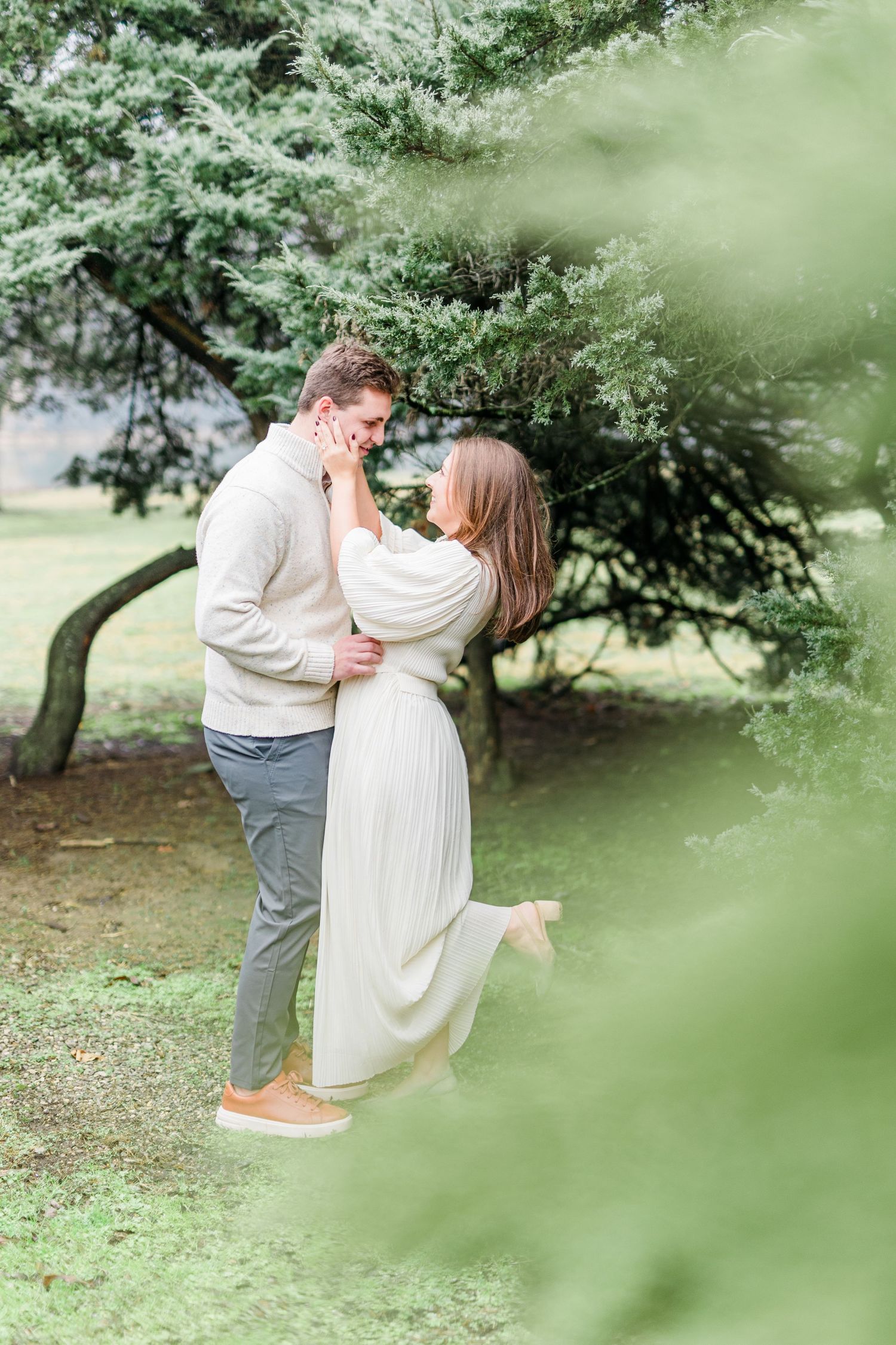 A romantic couple embraces in a garden setting with soft green foliage in the foreground.