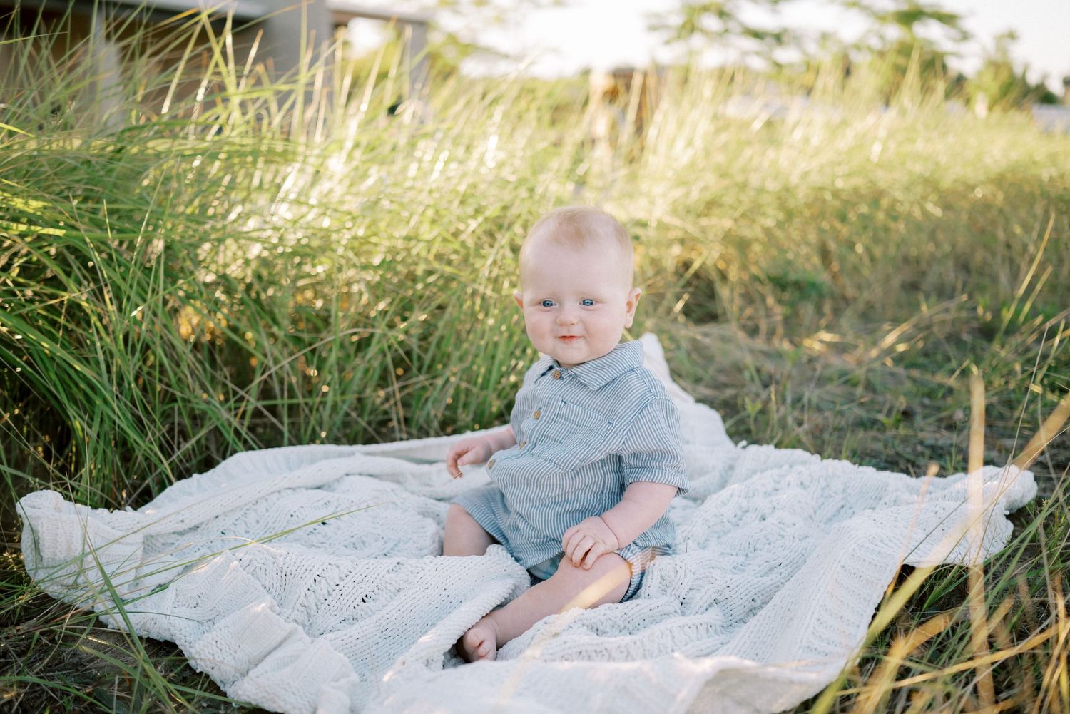 Small child sits on a white blanket surrounded by golden tall grass during sunset.