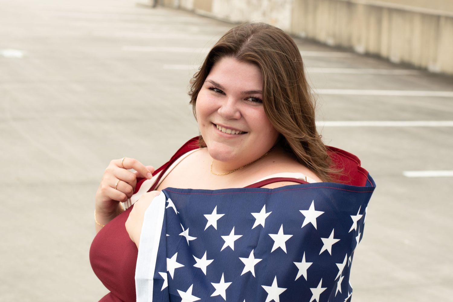 Woman in red top holding American flag with stars portion against concrete wall.