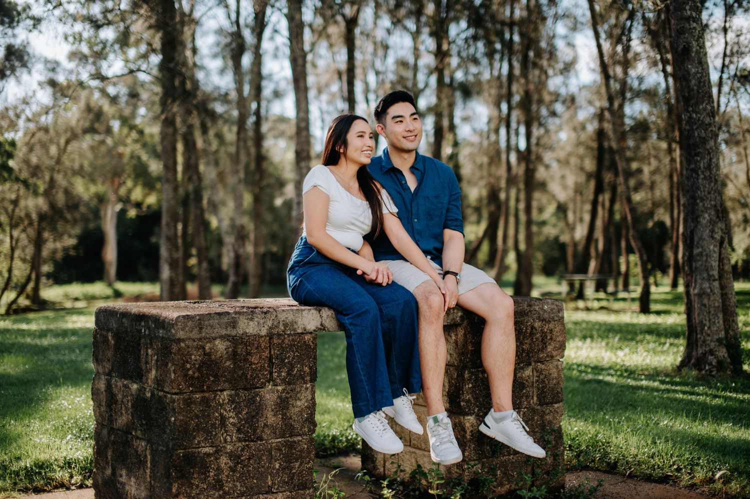 Couple sits together on rustic stone blocks in serene forest setting.