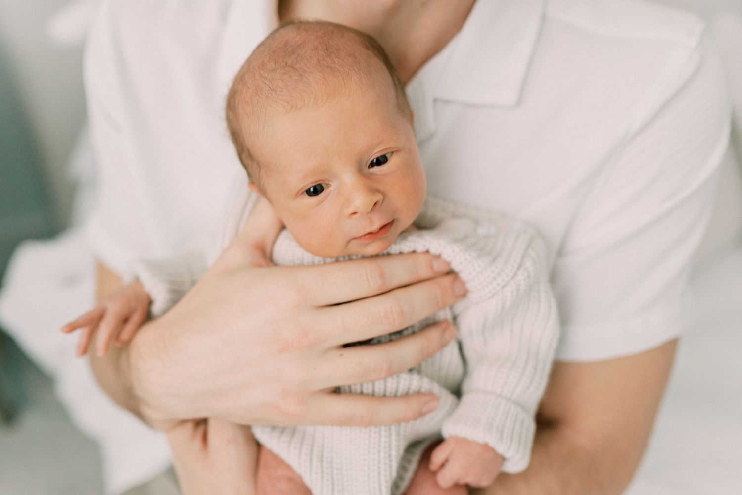 Newborn in white sweater being cradled in caring hands.