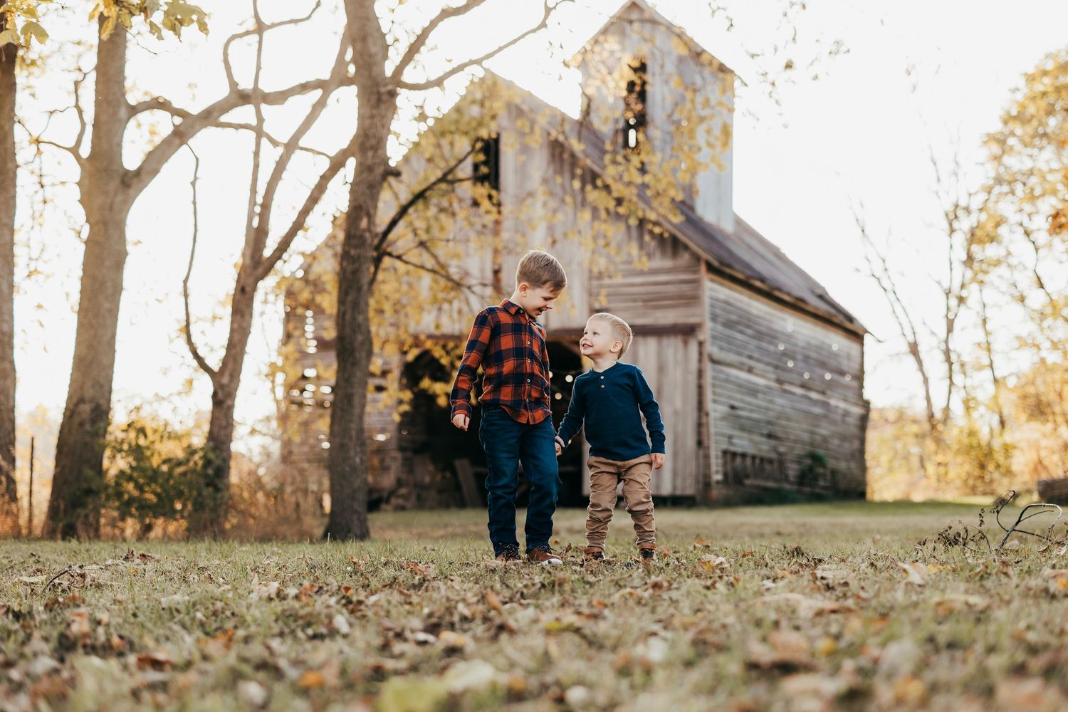 Two small children walk hand in hand towards a rustic old church on an autumn day in golden light.