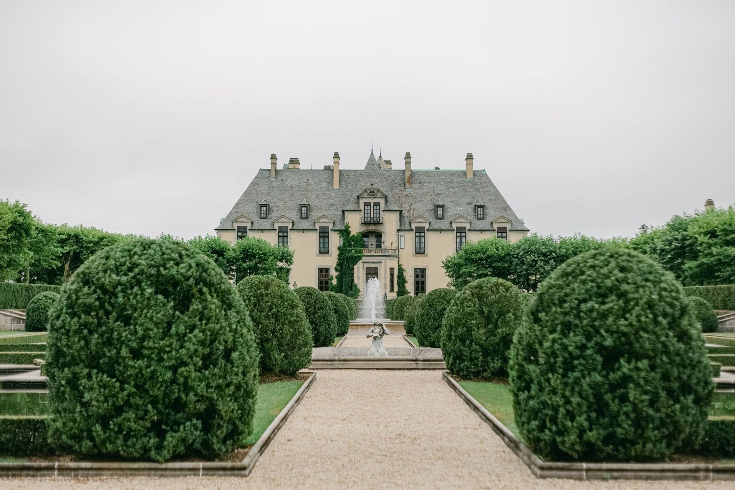 Elegant French manor house with manicured topiary gardens and a gravel path leading to the entrance.