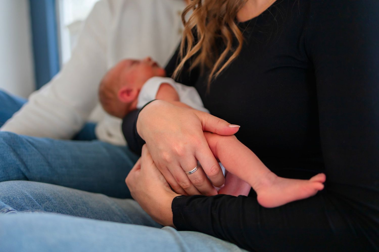 At home newborn photoshoot.  Mom and Dad torso in image, focus is on newborn sleeping in moms arms.