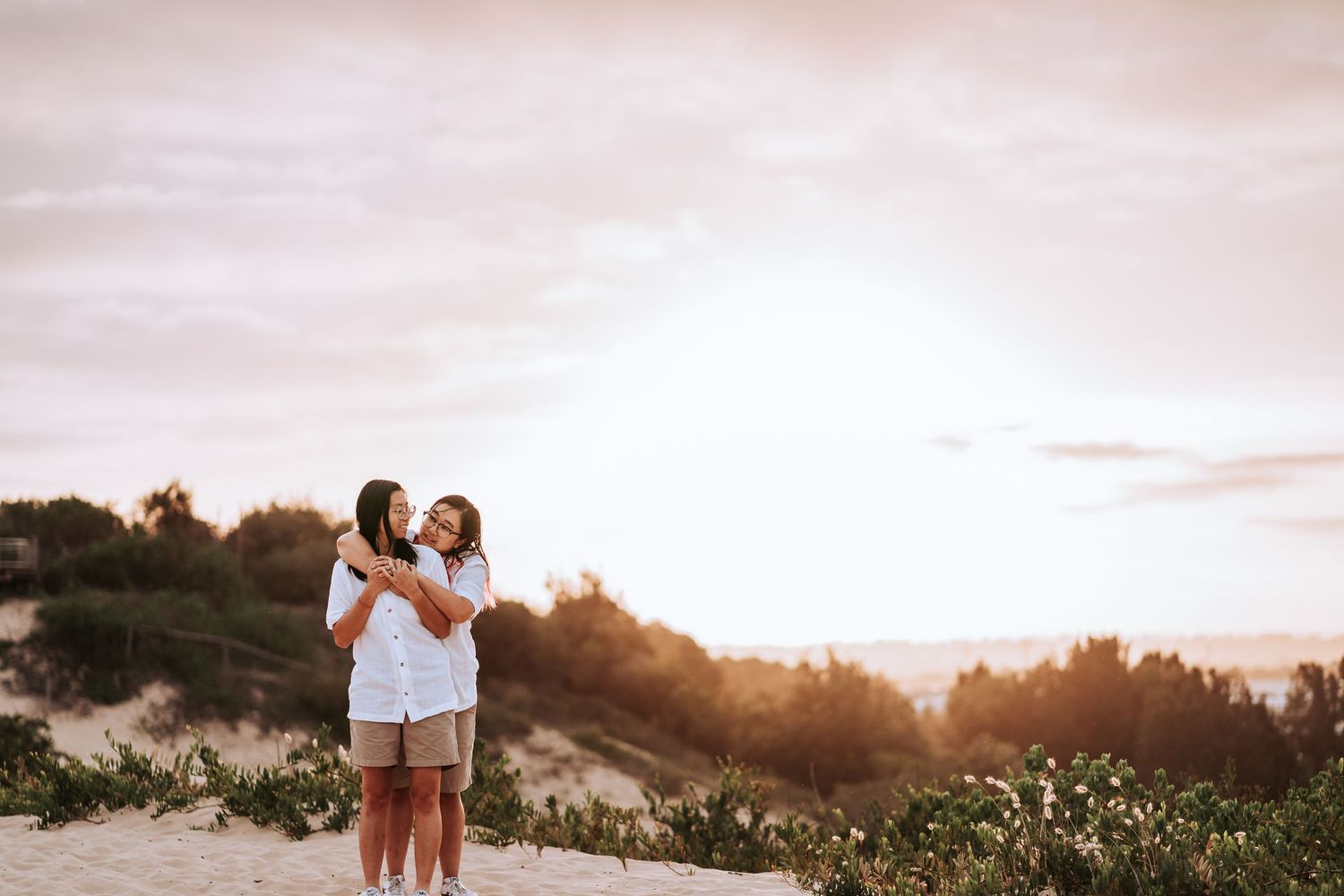 A couple embraces on a hilltop path surrounded by greenery during golden hour sunset.