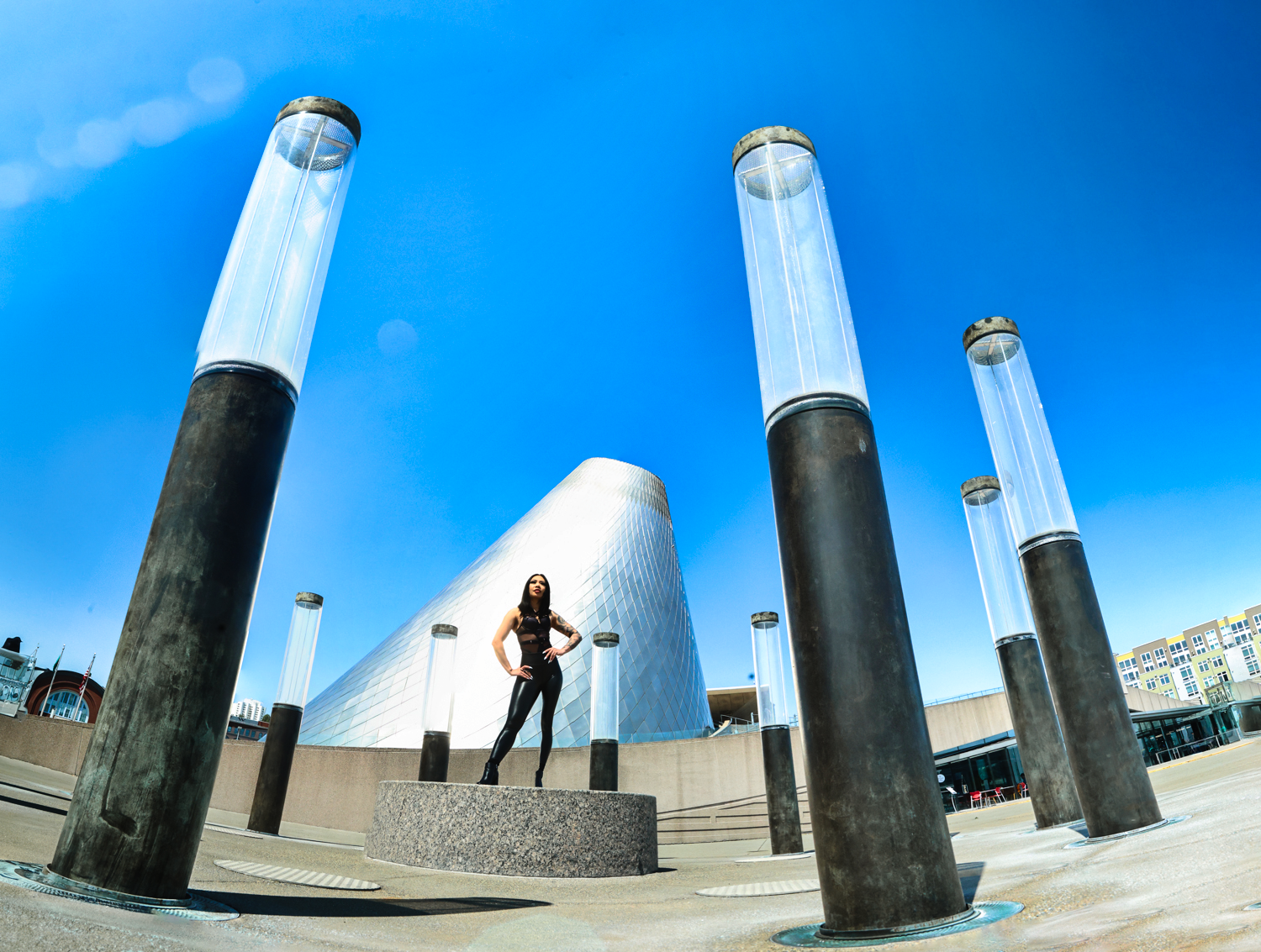 A silhouetted figure stands on a platform surrounded by tall cylindrical pillars against a bright blue sky.