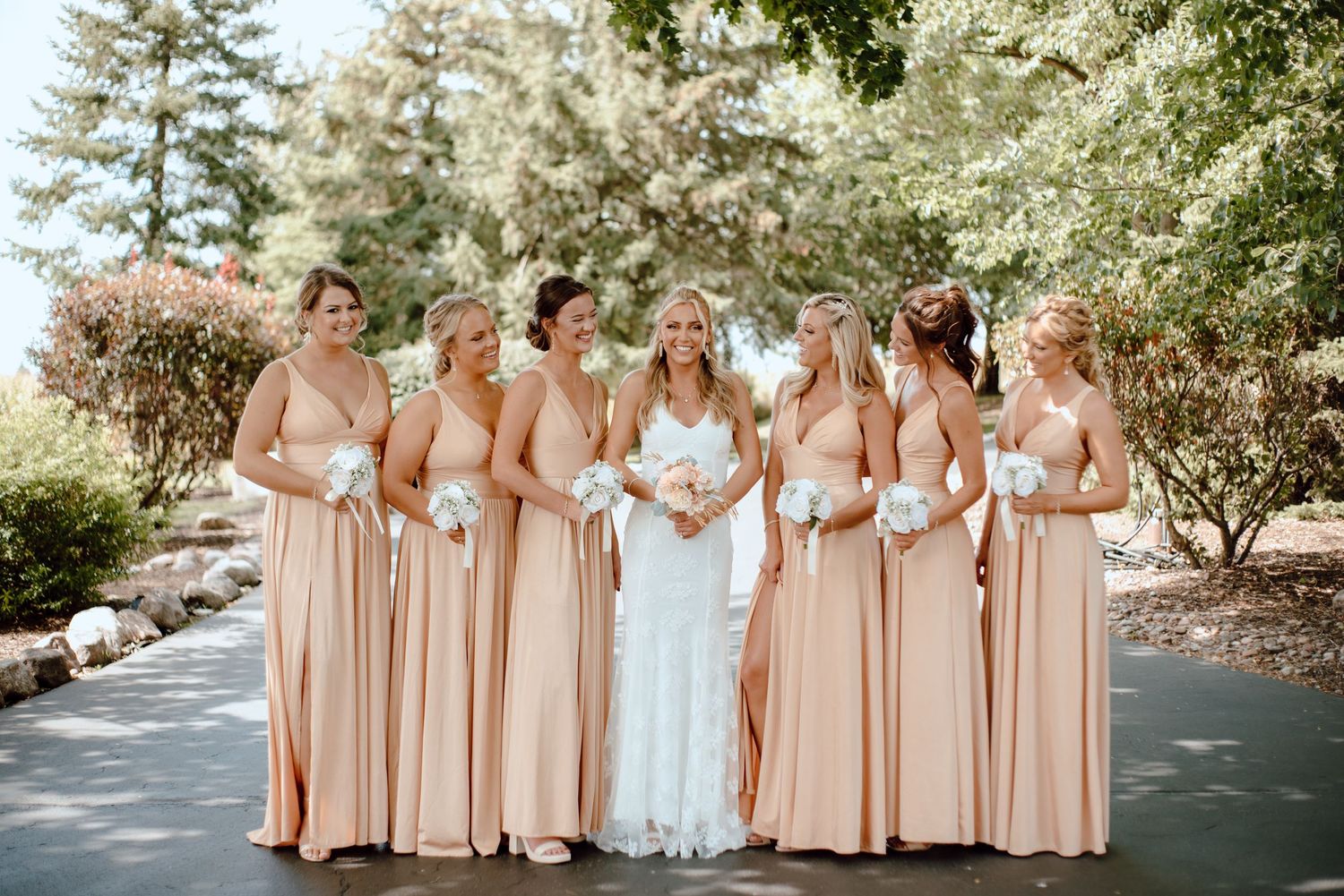 Bridal party in matching peach dresses poses outdoors among blooming trees.