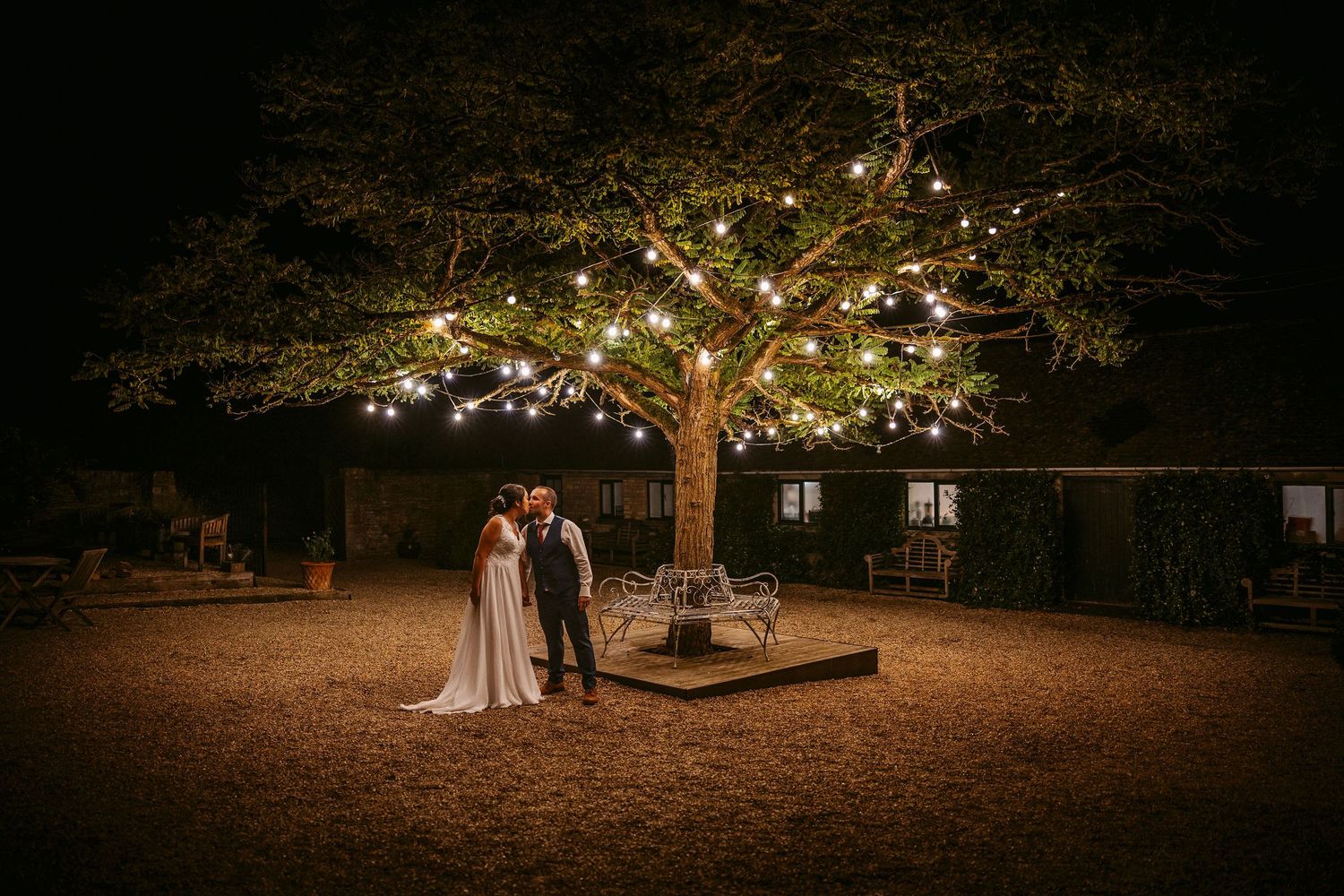 Merriscout wedding venue offers a romantic evening scene under a tree illuminated with string lights on a rustic outdoor ground.
