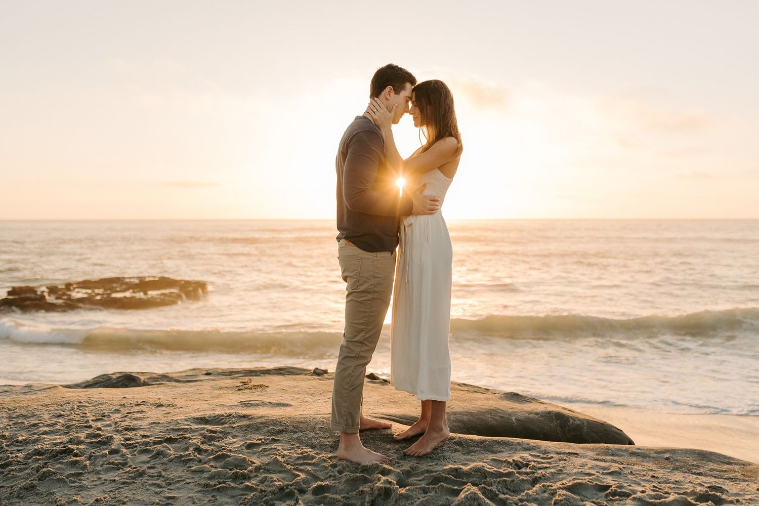 Couple shares intimate moment on rocky beach during golden hour at Windansea Beach in La Jolla.
