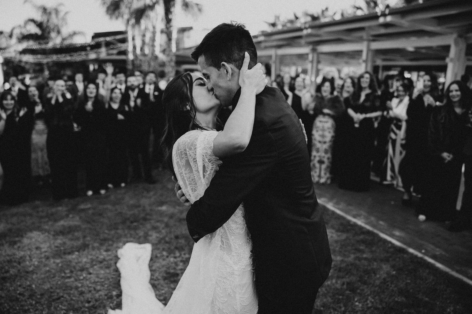 Wedding couple embraces in front of coral colored wall while holding a delicate bouquet.