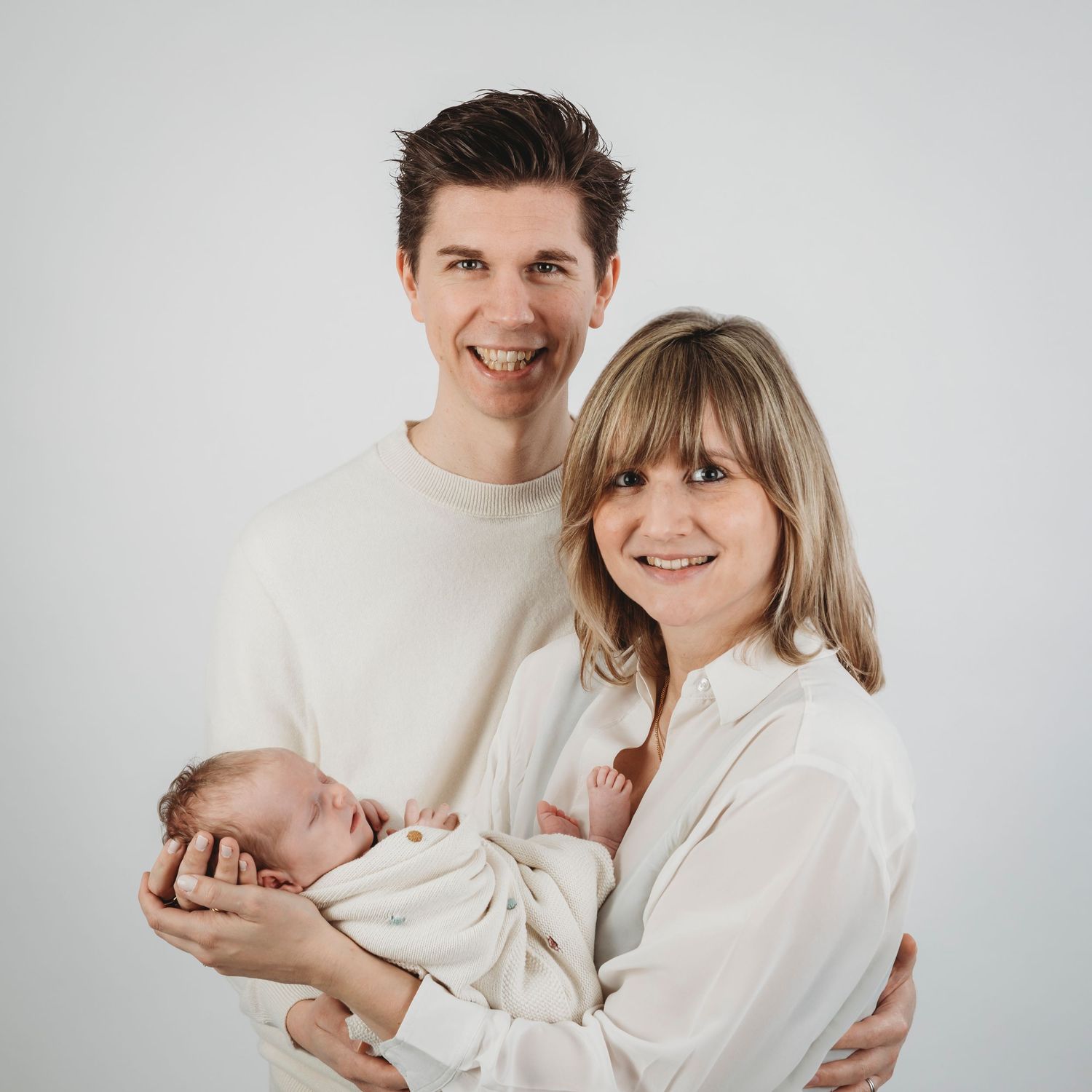Studio family portrait against white background in neutral tones.