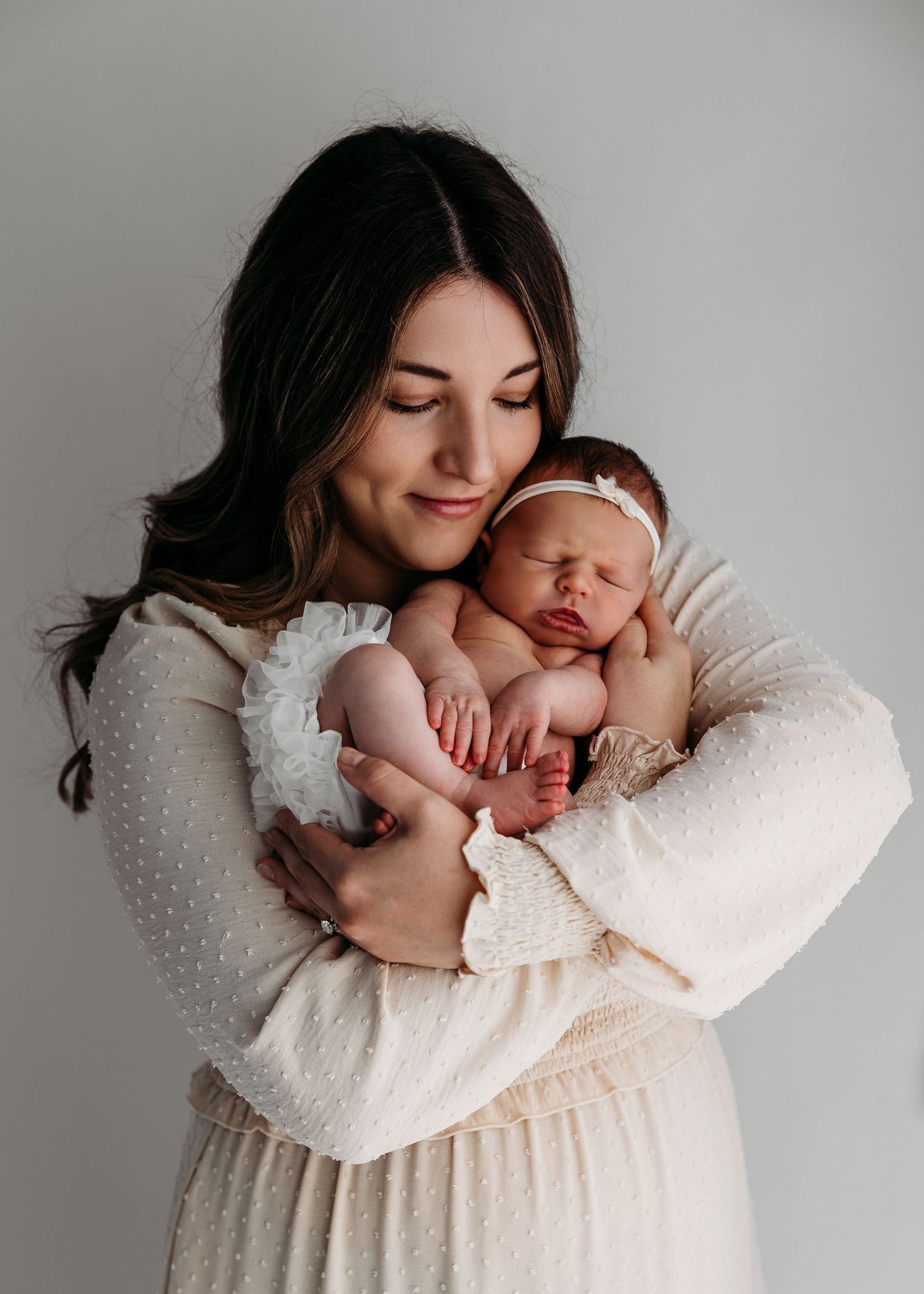 Professional portrait of parent holding sleeping newborn baby in white outfit.