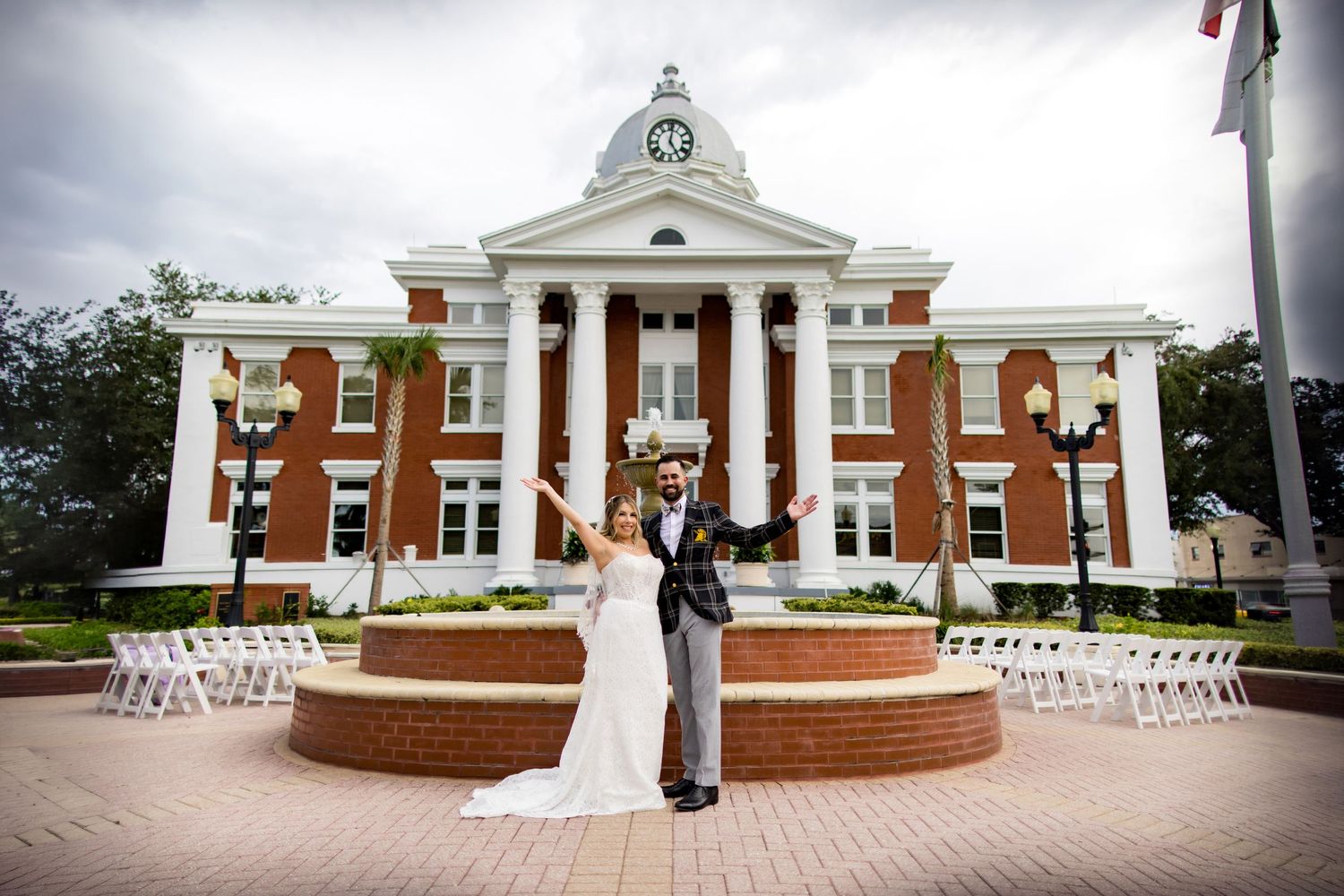Bride and groom celebrate with arms raised outside a grand brick courthouse with white columns on their wedding day.