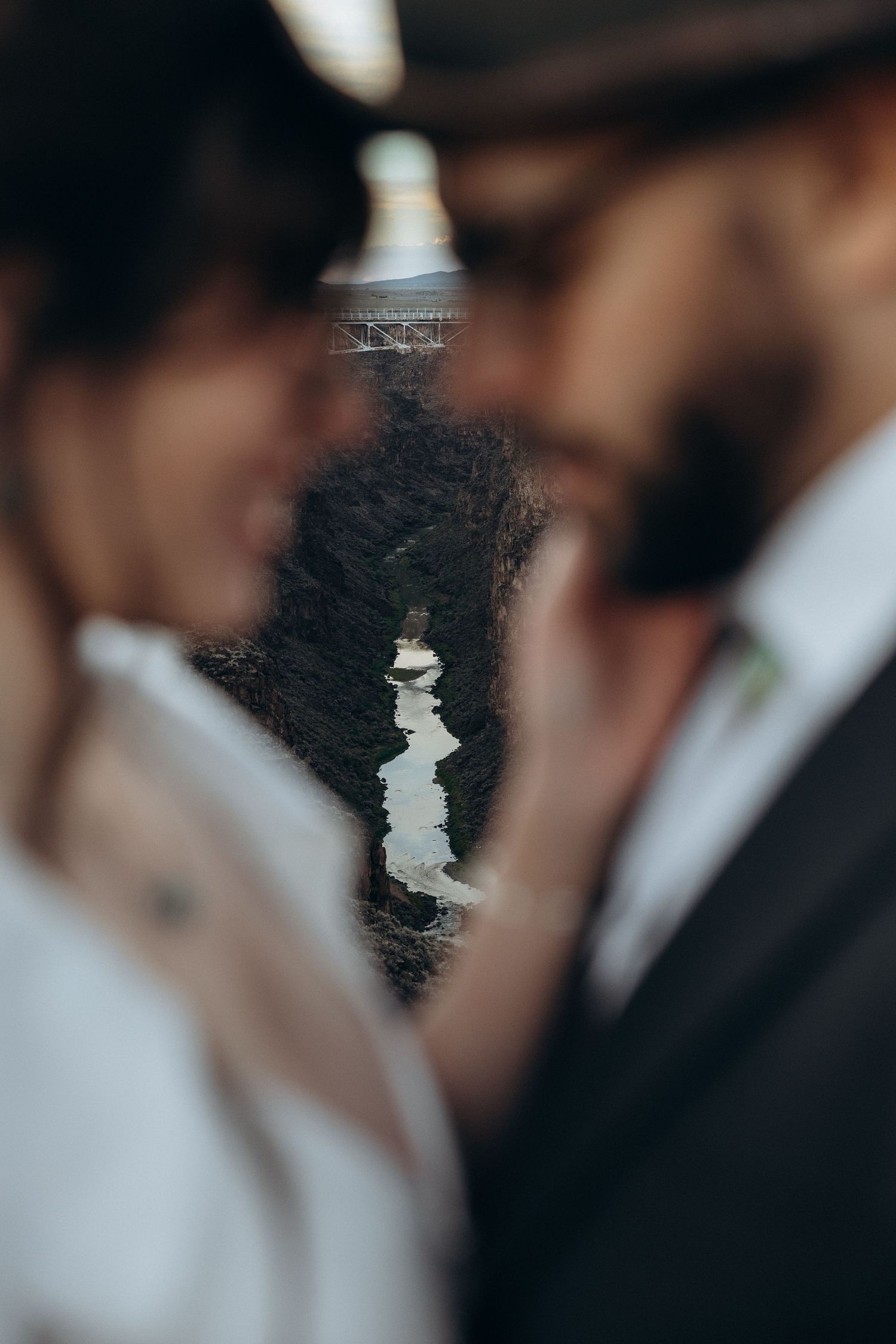 Couple sharing romantic moment in wedding attire with bouquet, Rio Grande Gorge Bridge in background, New Mexico.