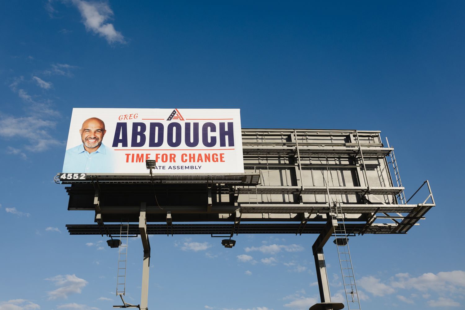 Billboard against a blue sky reading Abdouch, Time for Change, State Assembly, with a smiling man's portrait in a campaign advertisement.