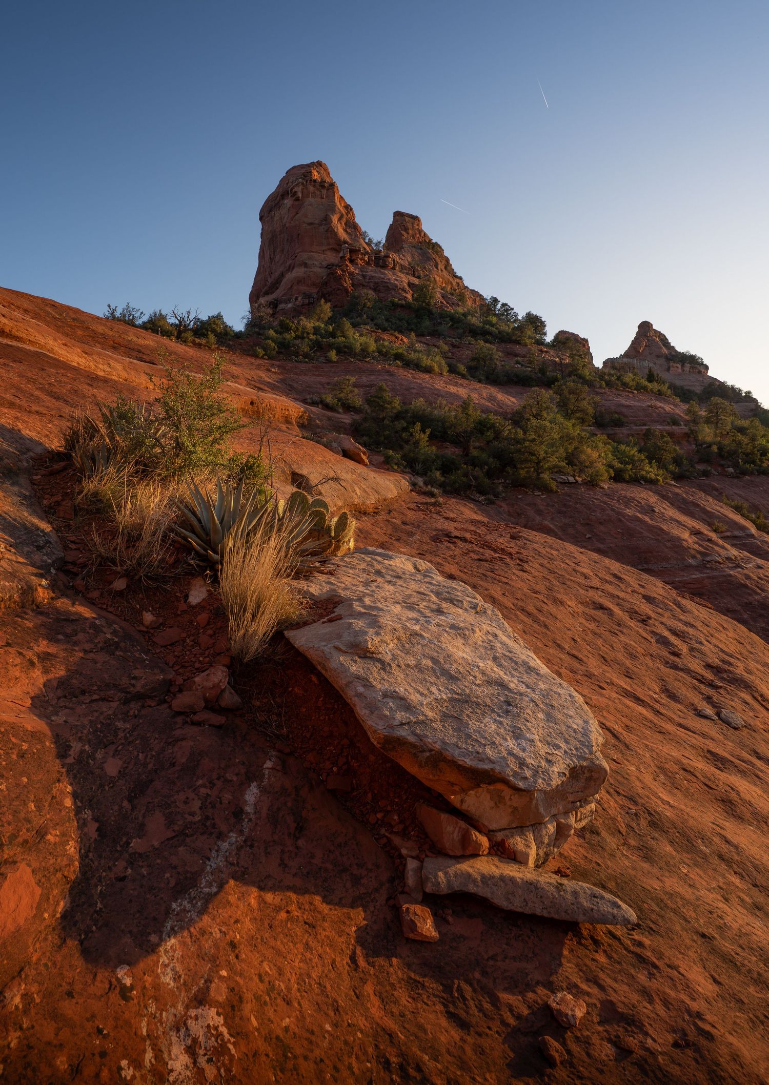 A series of silhouetted figures stand against a sunset sky viewed through natural rock arches in a desert landscape.