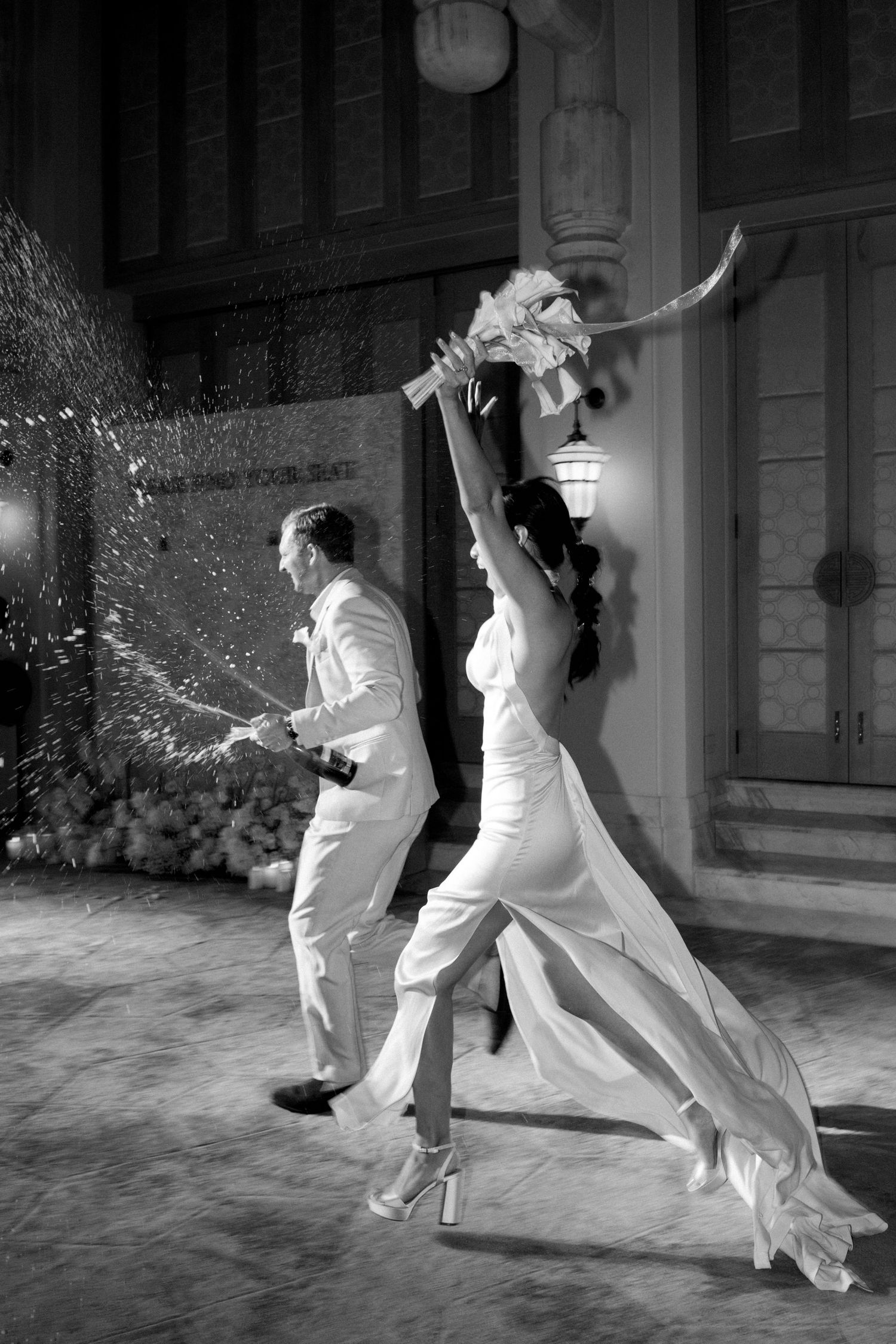 Two dancers in white outfits perform an elegant dance sequence together in black and white at night outside a building.
