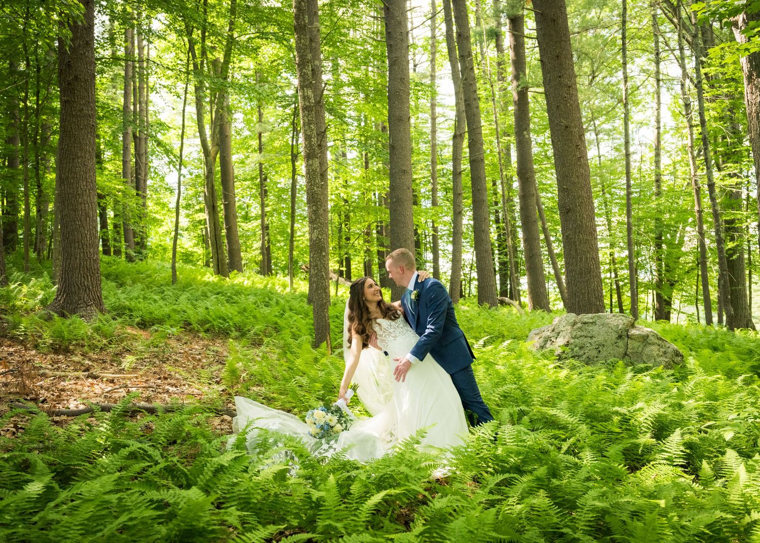 Newlyweds share an intimate moment outdoors with autumn foliage and rustic architecture in background.