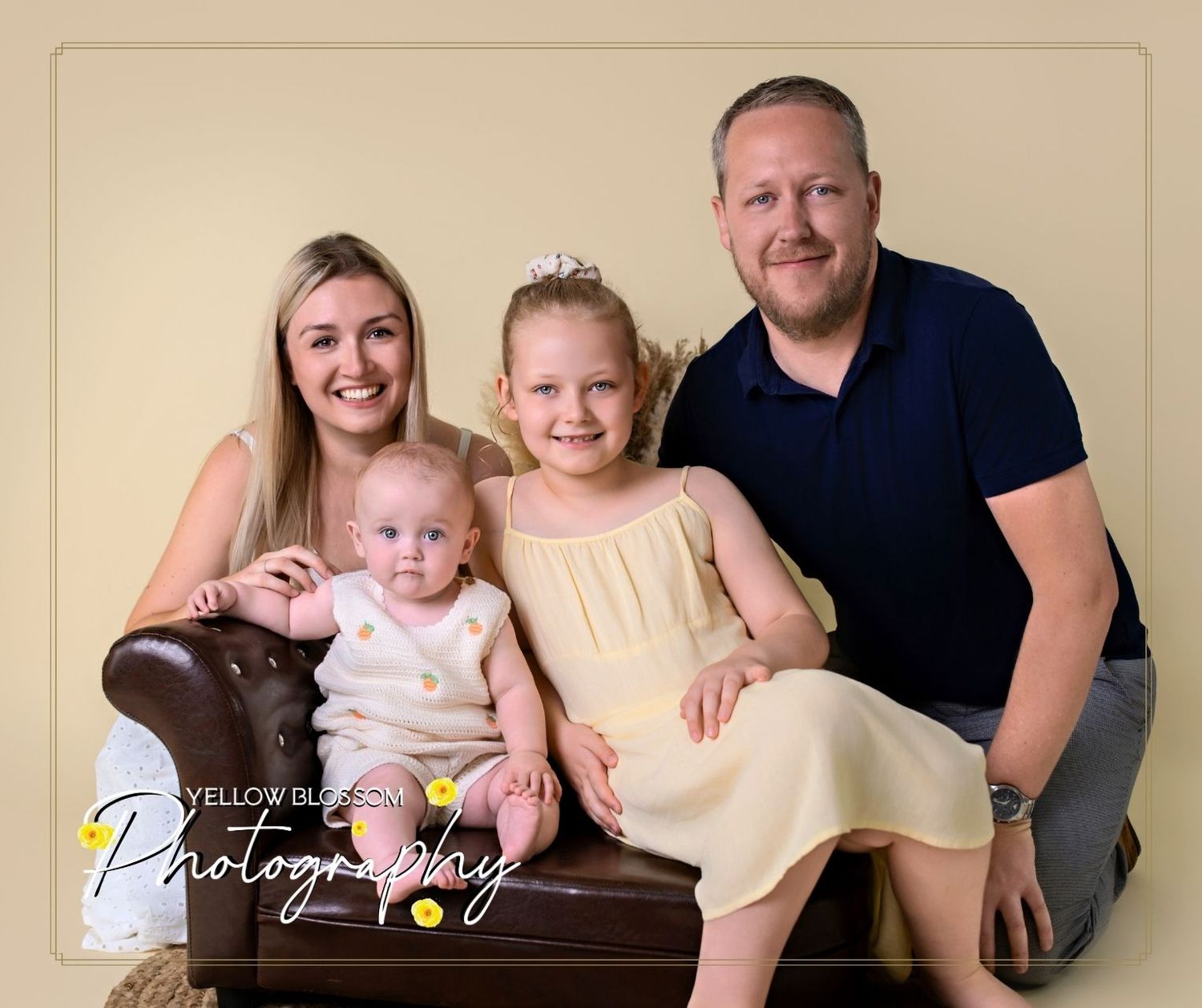 A family of four sits together for a professional studio portrait against a neutral background. Haverhill, Suffolk