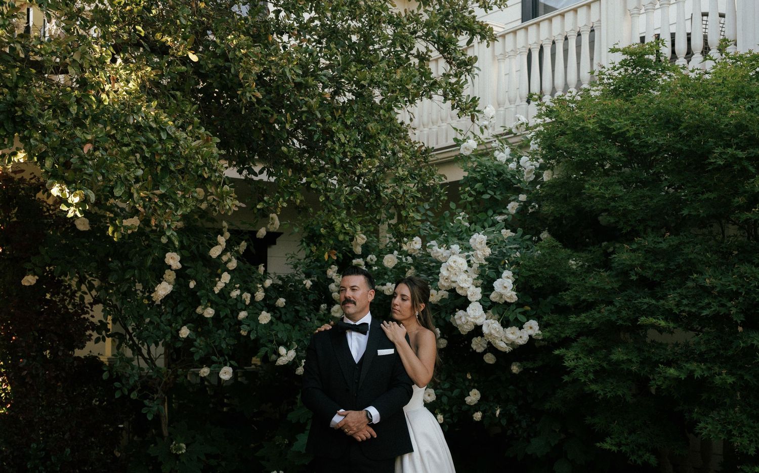 Black and white outdoor wedding ceremony with rows of chairs and white umbrellas in front of a charming countryside house.