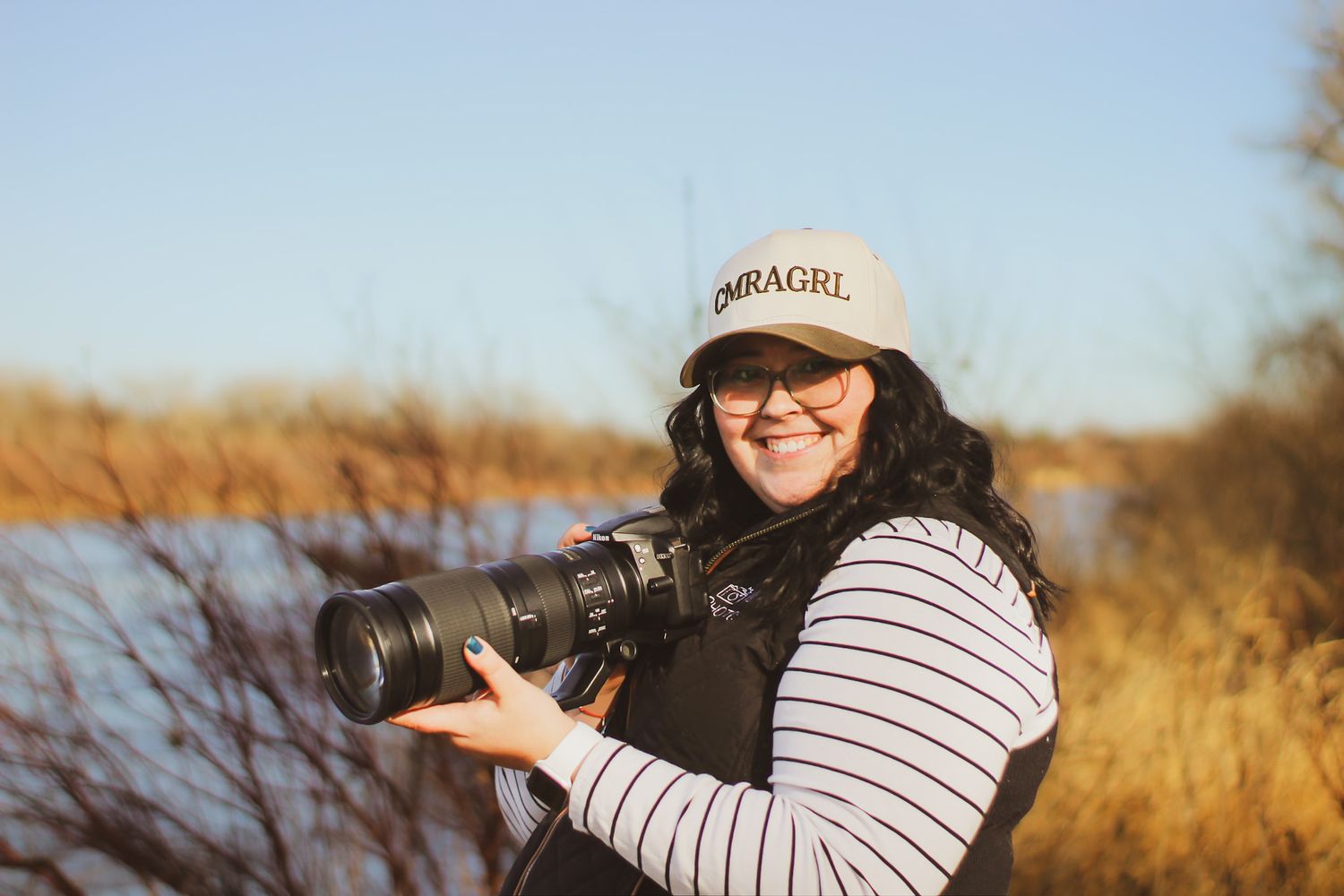 Wildlife photographer wearing a striped shirt and baseball cap photographs birds in a golden autumn field.
